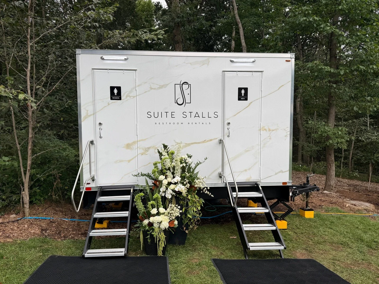 Suite Stalls restroom trailer with a tall white floral arrangement, shown from the front at a black tie event.