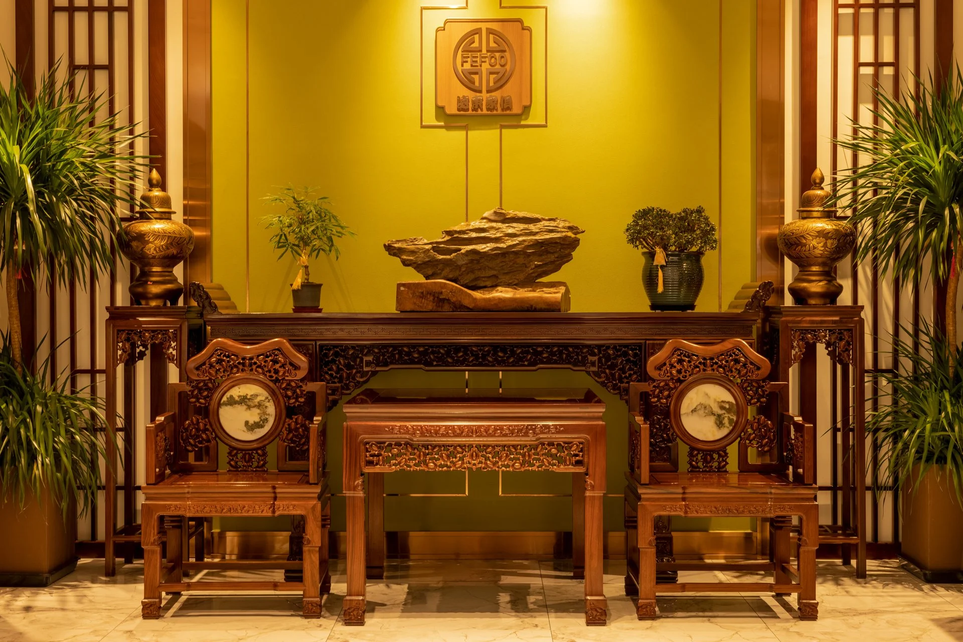 A traditional Chinese interior with carved wooden furniture, ornamental plants, and decorative items.