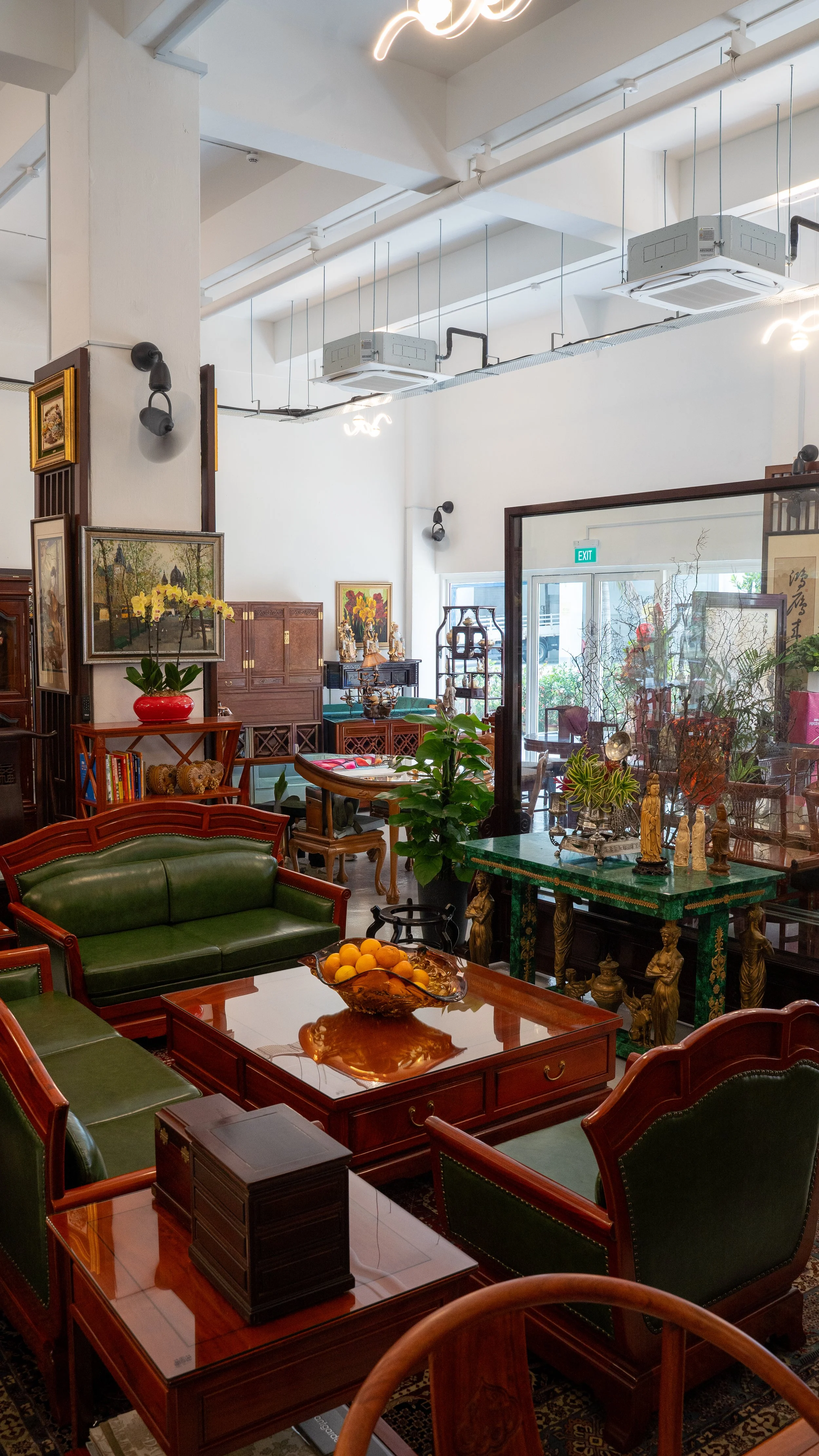 Interior of an antique shop with wooden furniture, paintings, and decorative items on display, lit with ceiling lights and natural light from a glass door.