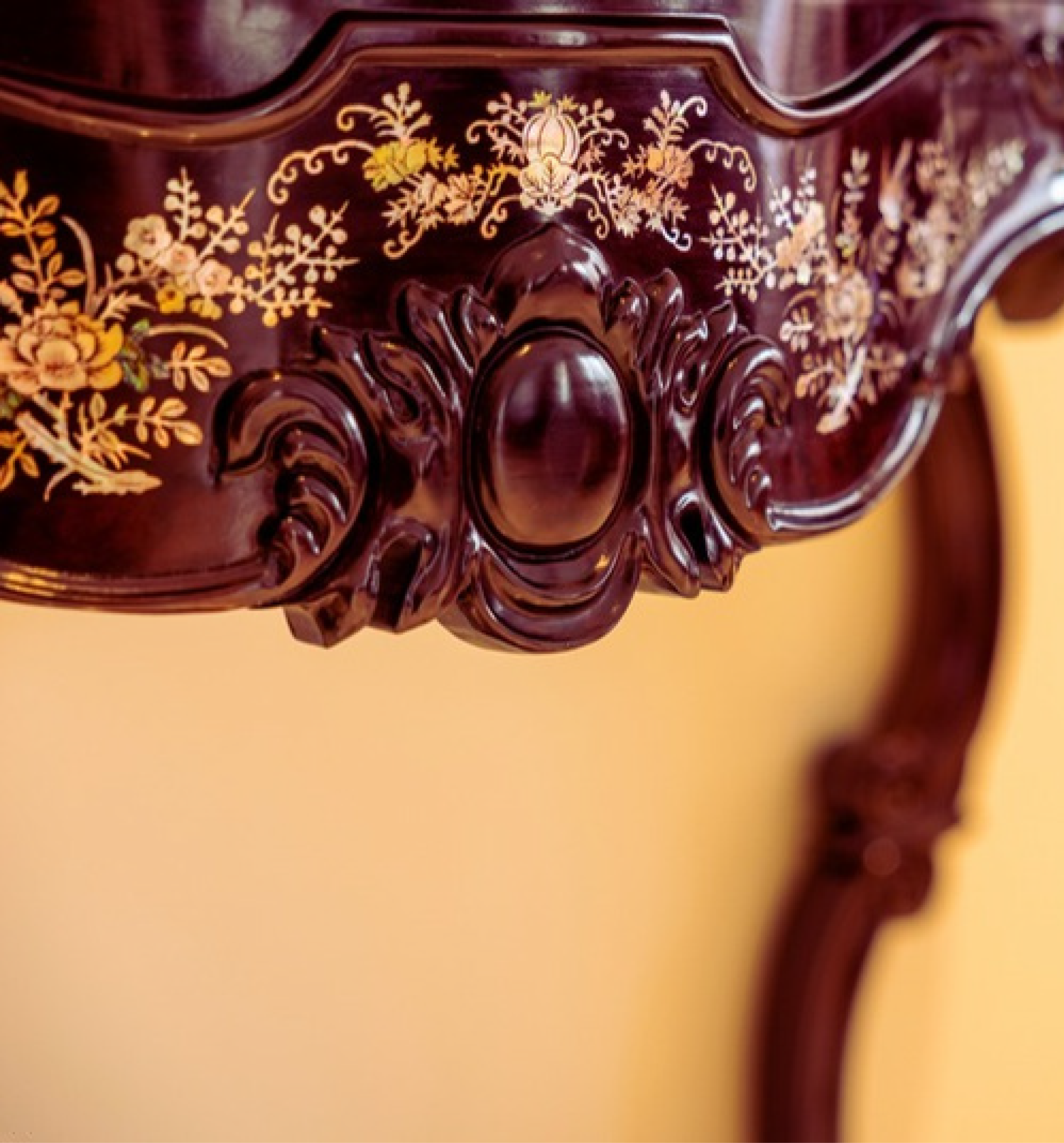 Close-up of an ornate, dark wood antique chair with gold floral inlay carvings on the backrest.