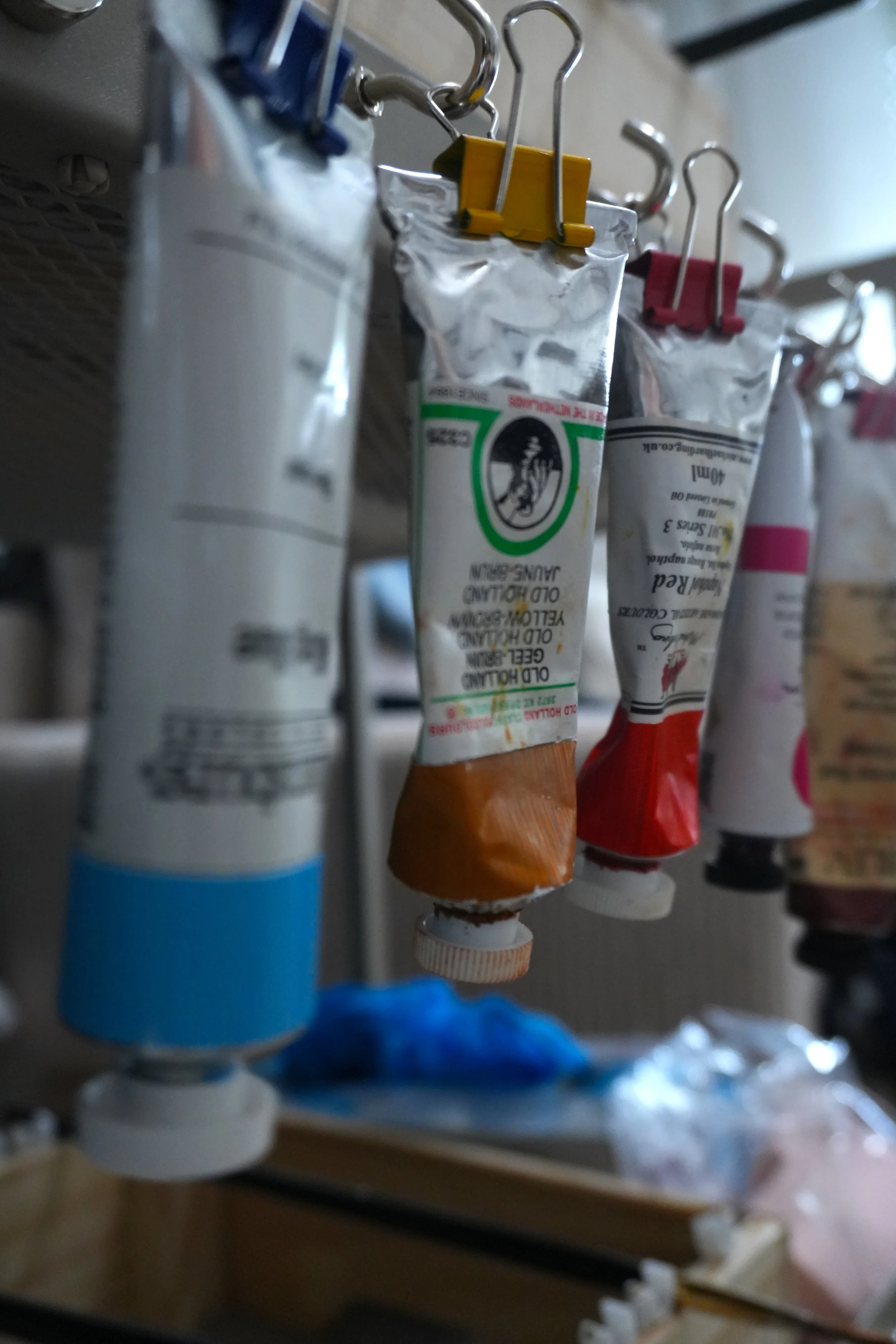 Close-up of used squeeze tubes of oil paint hanging in a row, with a blurred background.