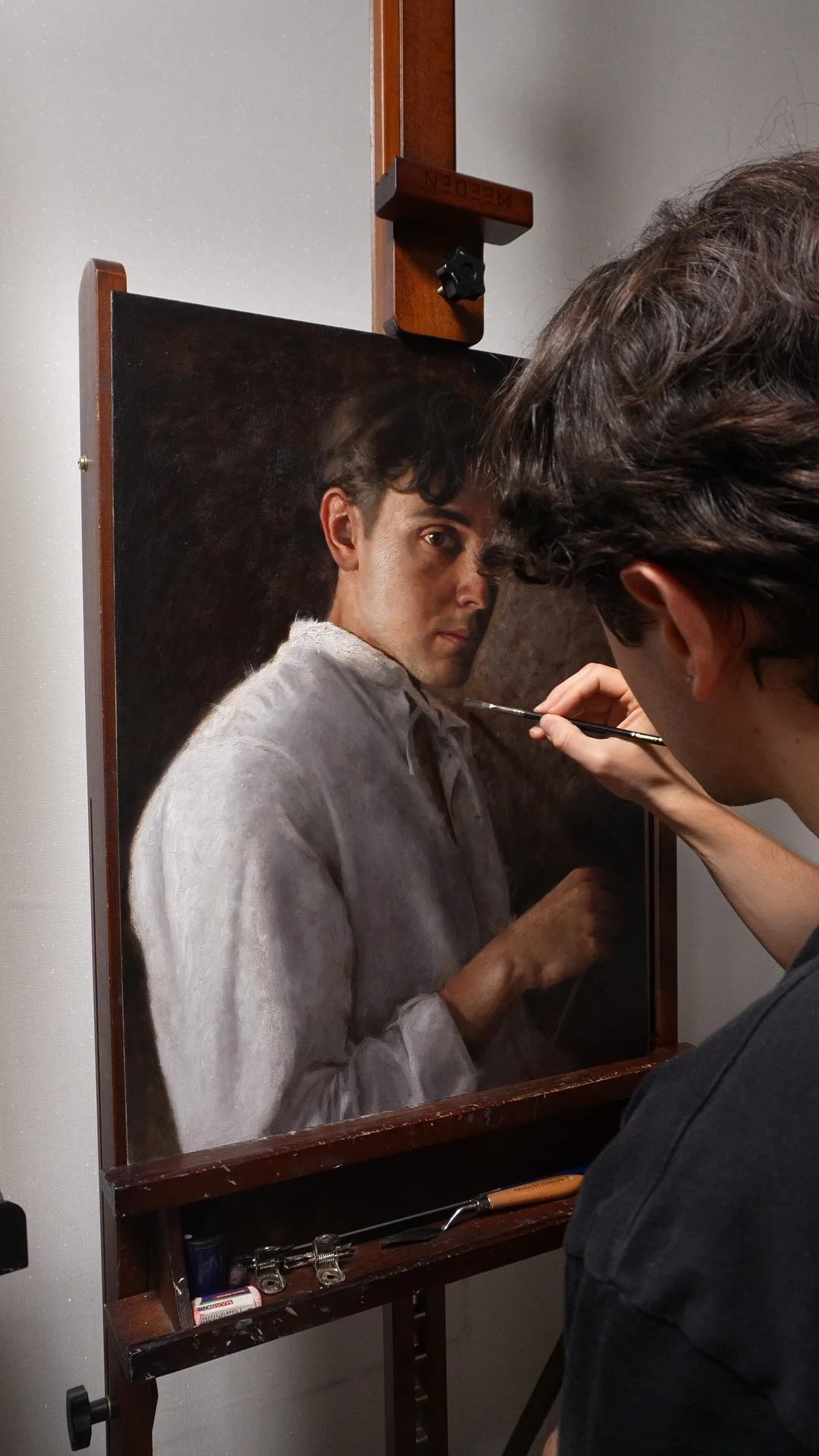 An artist is painting a self-portrait on an ACM Panel, capturing intricate details of his face and white shirt.