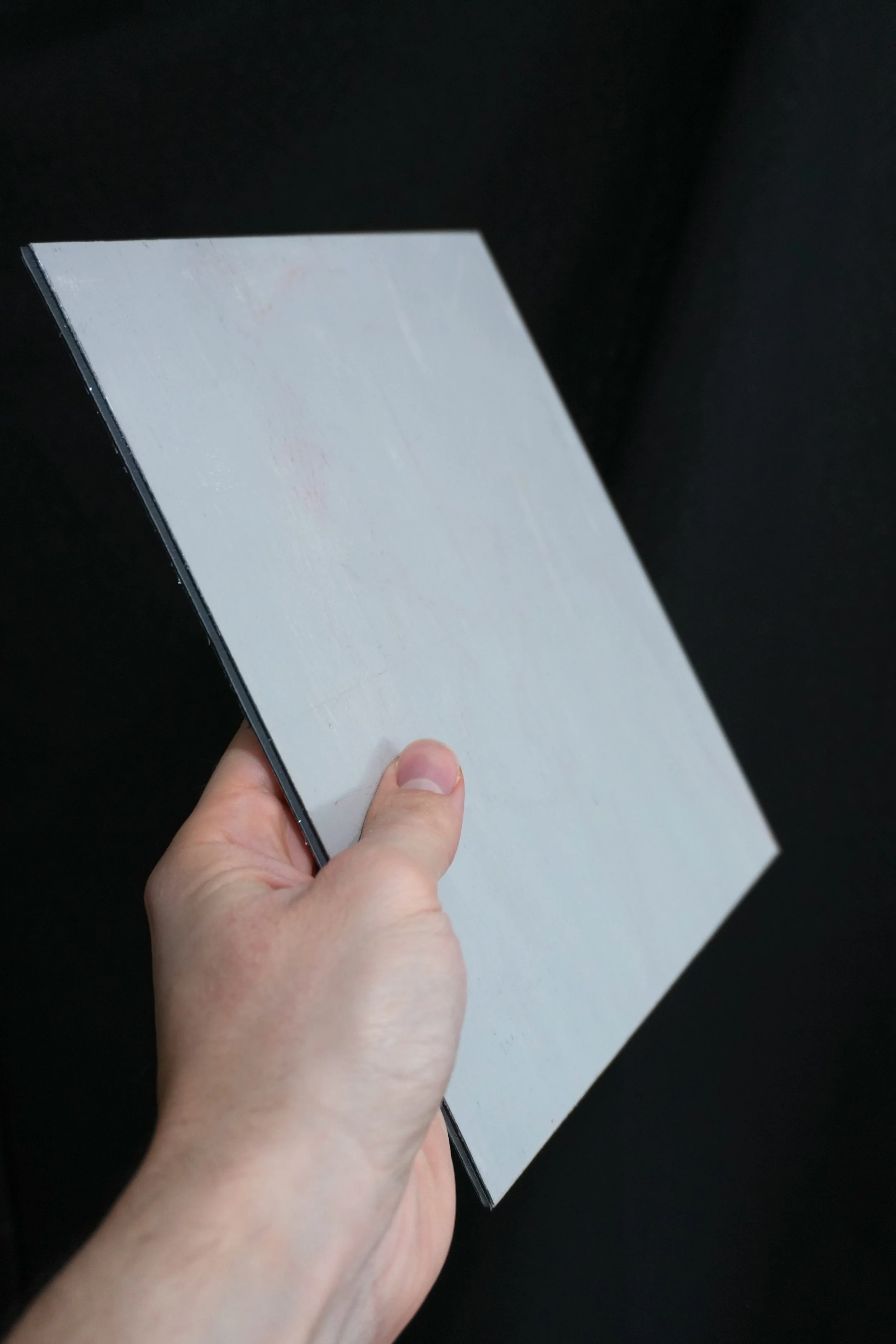 Hand holding an ACM panel against a black background.