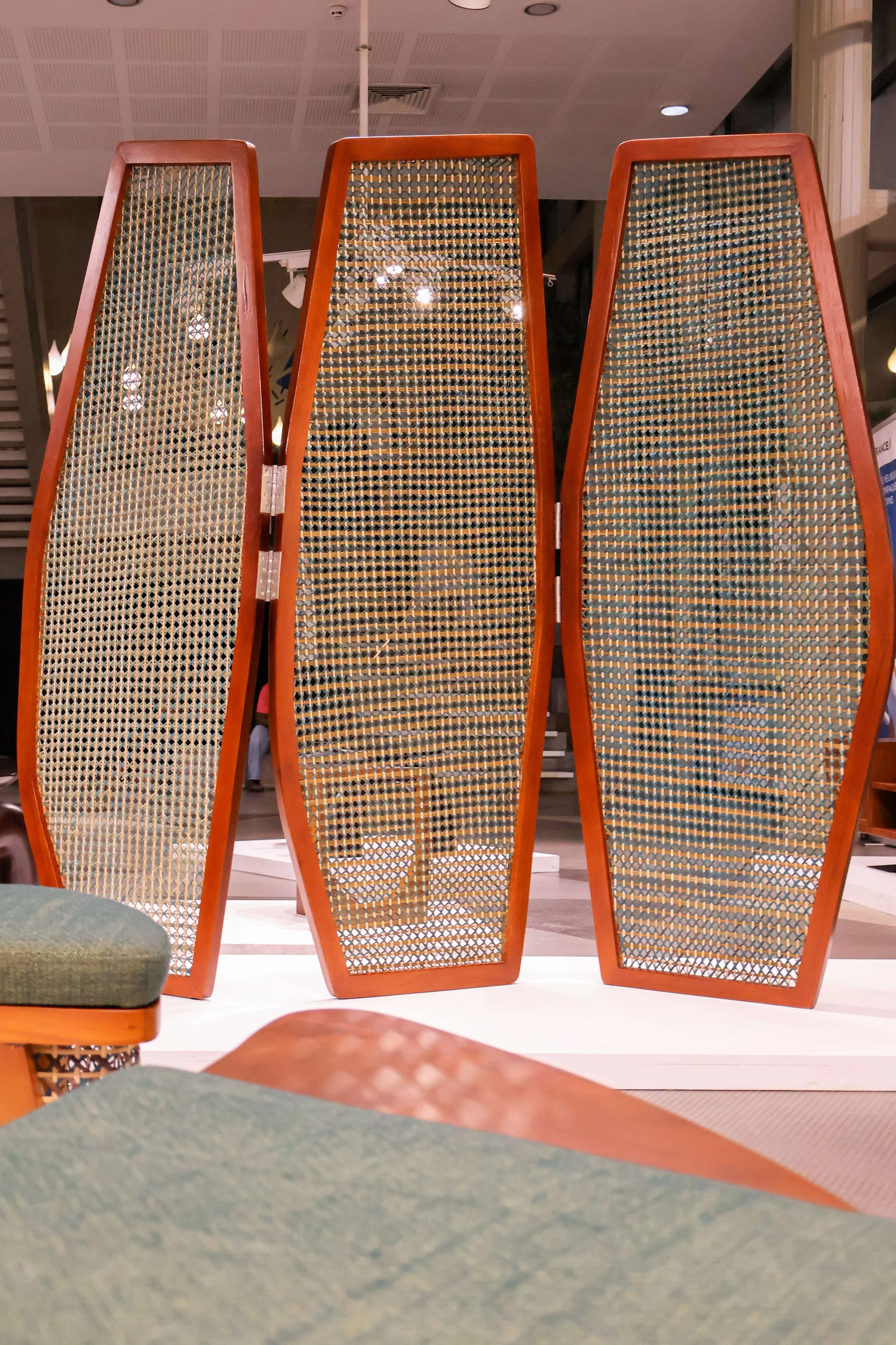 A decorative room divider with three tall, narrow panels made of wood and woven cane panels.