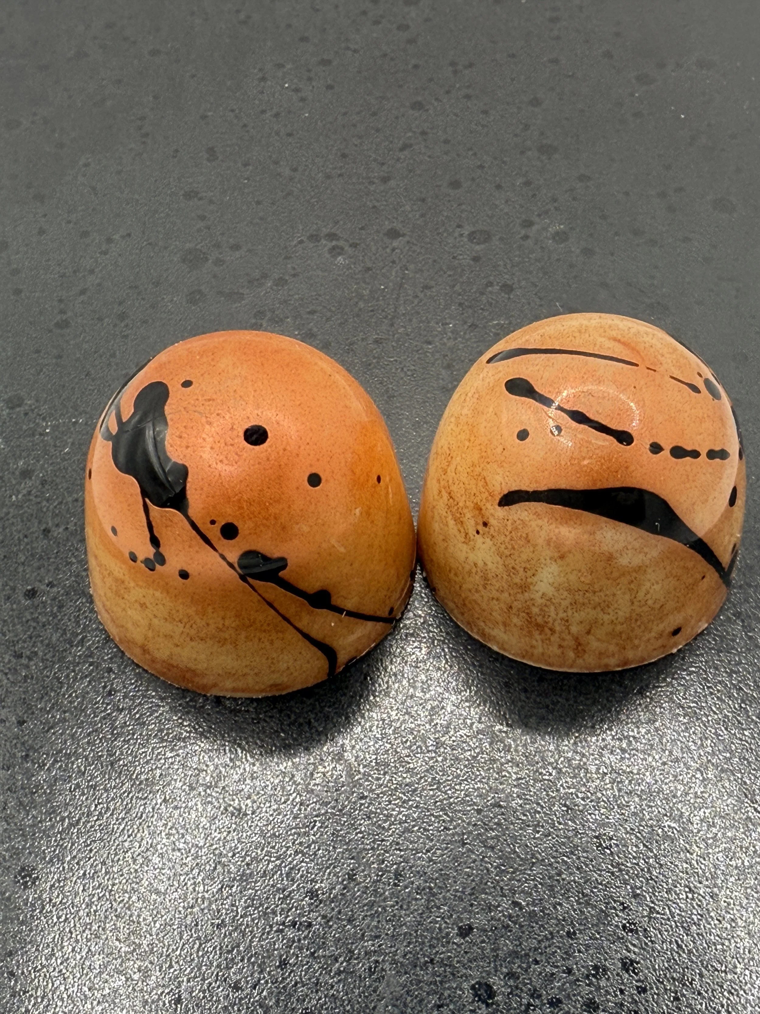 Two hand painted artisan filled bonbon chocolates with abstract black lines and dots on a dark surface.