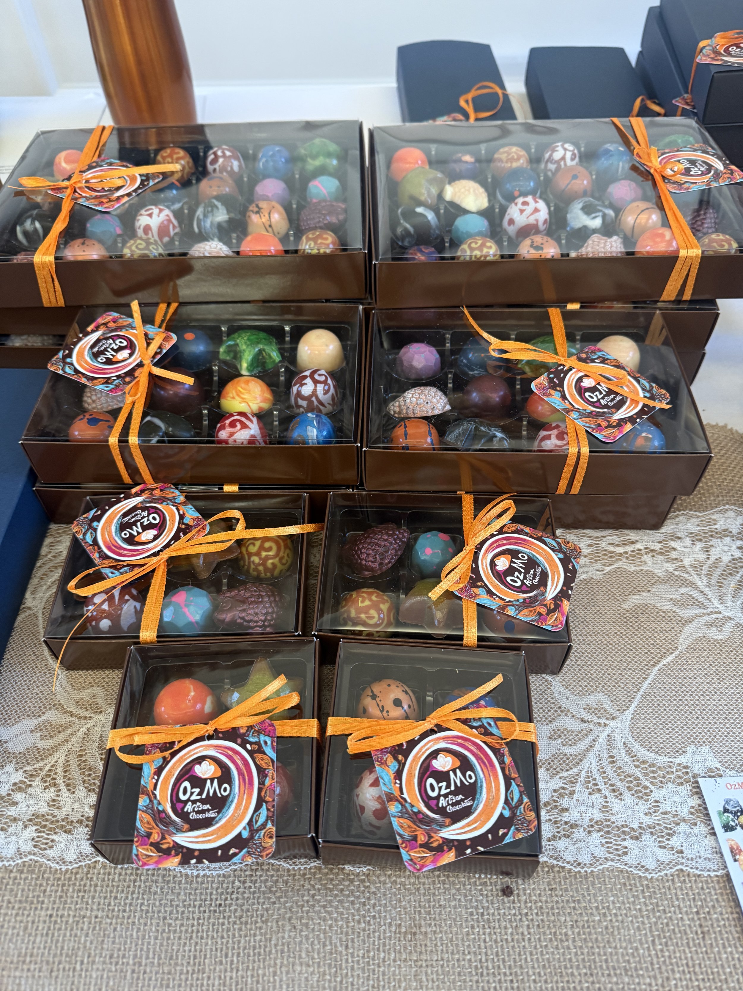 Luxury boxes of assorted artisan hand decorated chocolates wrapped with orange ribbons, placed on a lace-covered table.