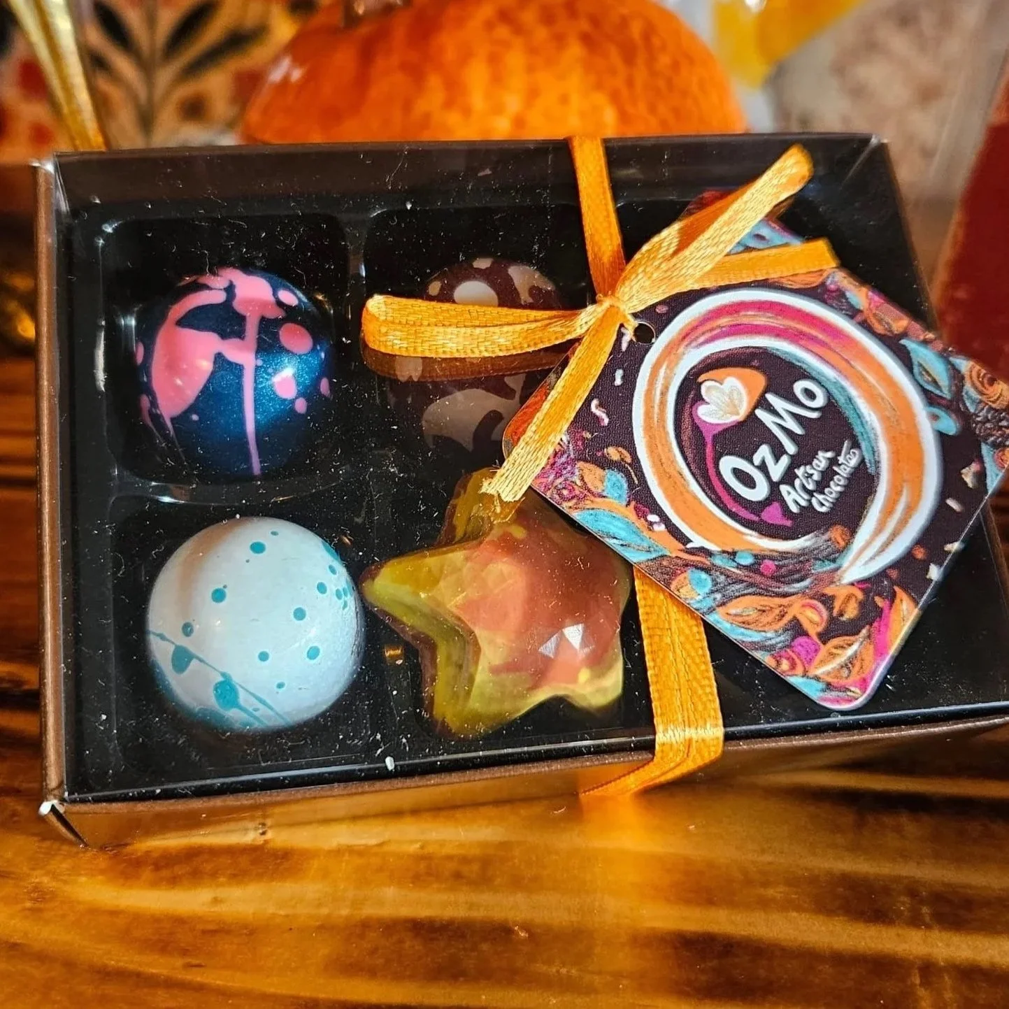 A box of decorated chocolates and candies, including a star-shaped,, with a decorative tag tied with an orange ribbon.