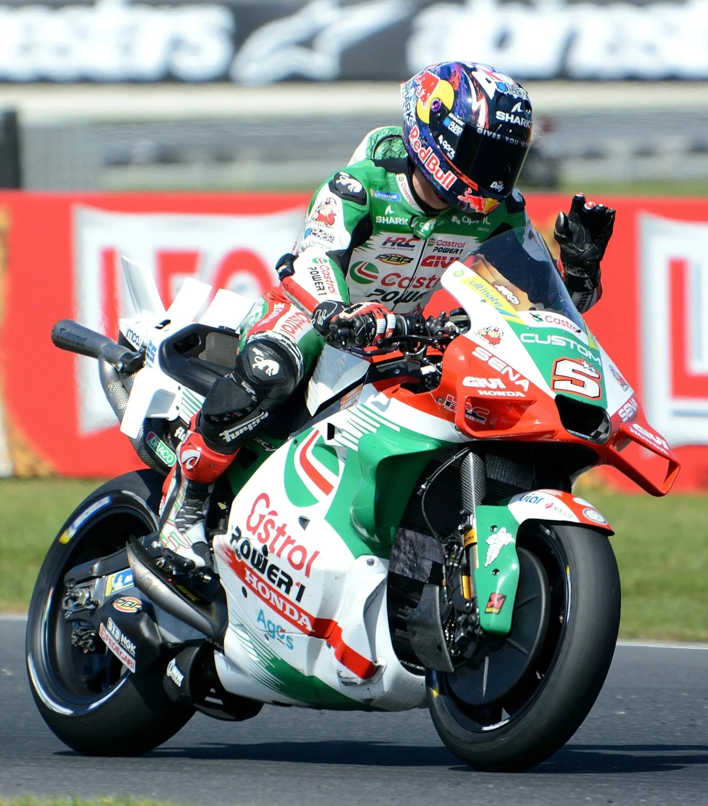 A motorcycle racer wearing a Dressel helmet, racing suit, and gloves, riding a Honda racing motorcycle decorated with Castrol and other sponsor logos on a race track.