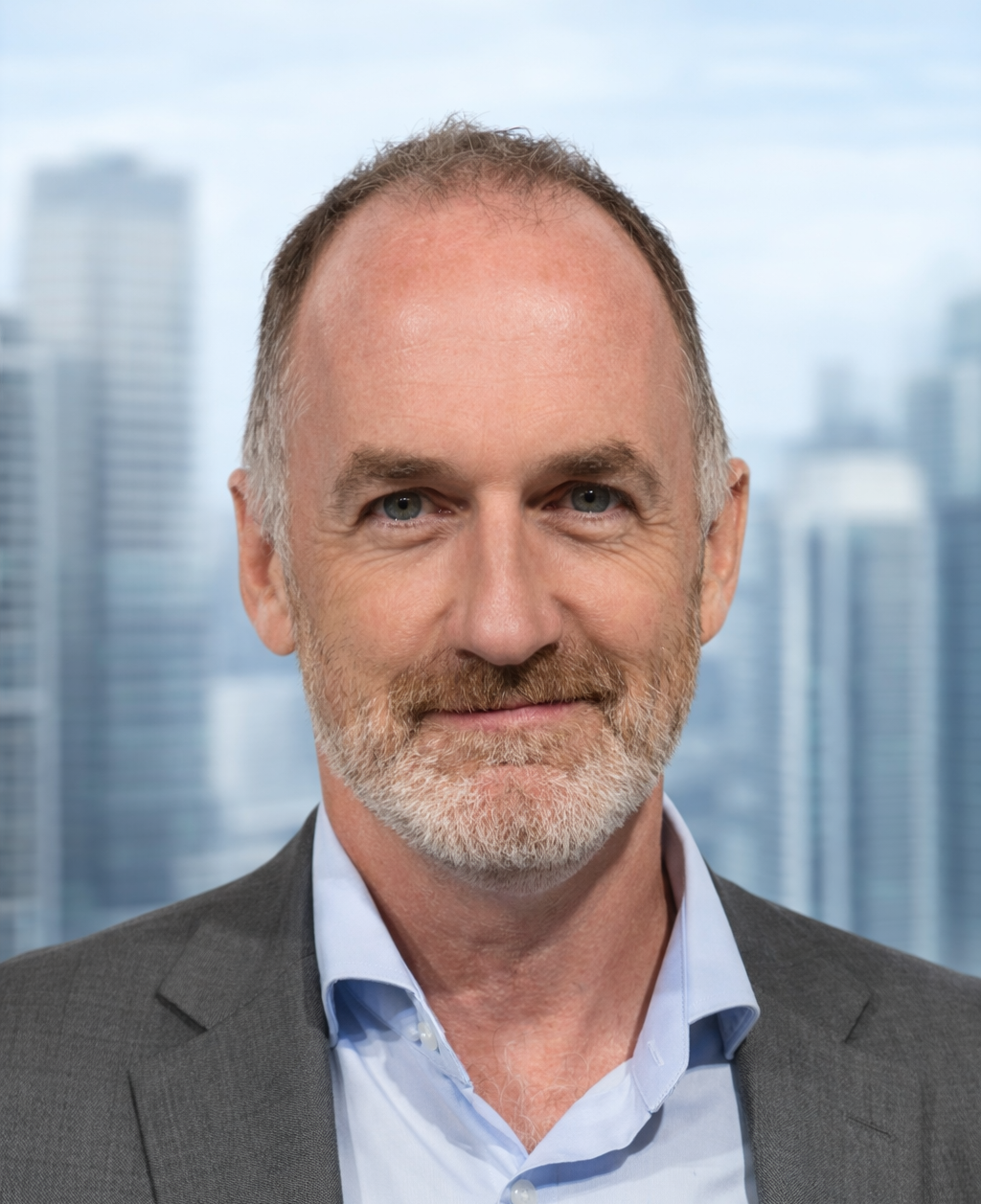 Close-up portrait of a middle-aged man with a beard, wearing a gray suit and light blue shirt, standing against a blurred cityscape background.