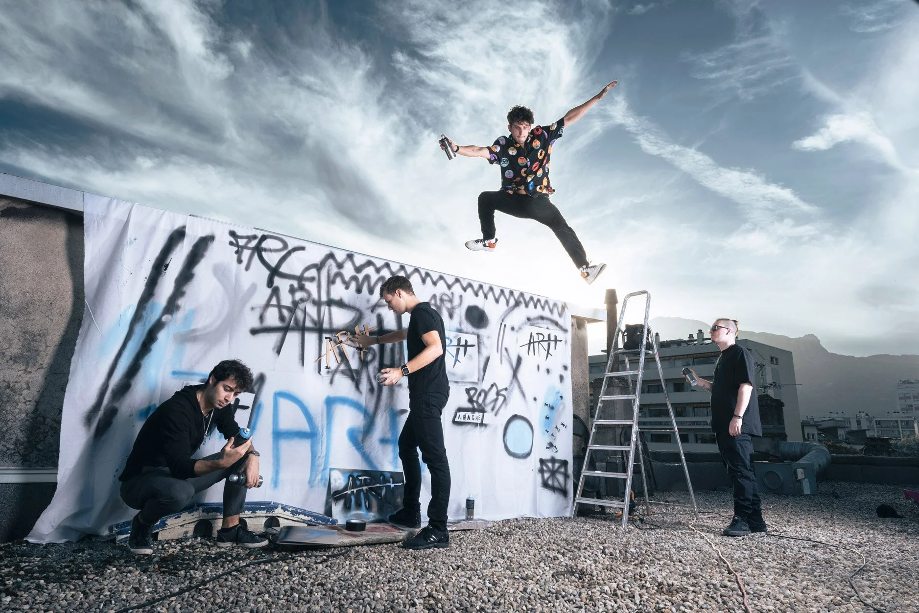 Un groupe de jeunes artistes graffeurs colorant un mur avec des bombes de peinture, avec l'un d'eux sautant en l'air sur un toit urbain.