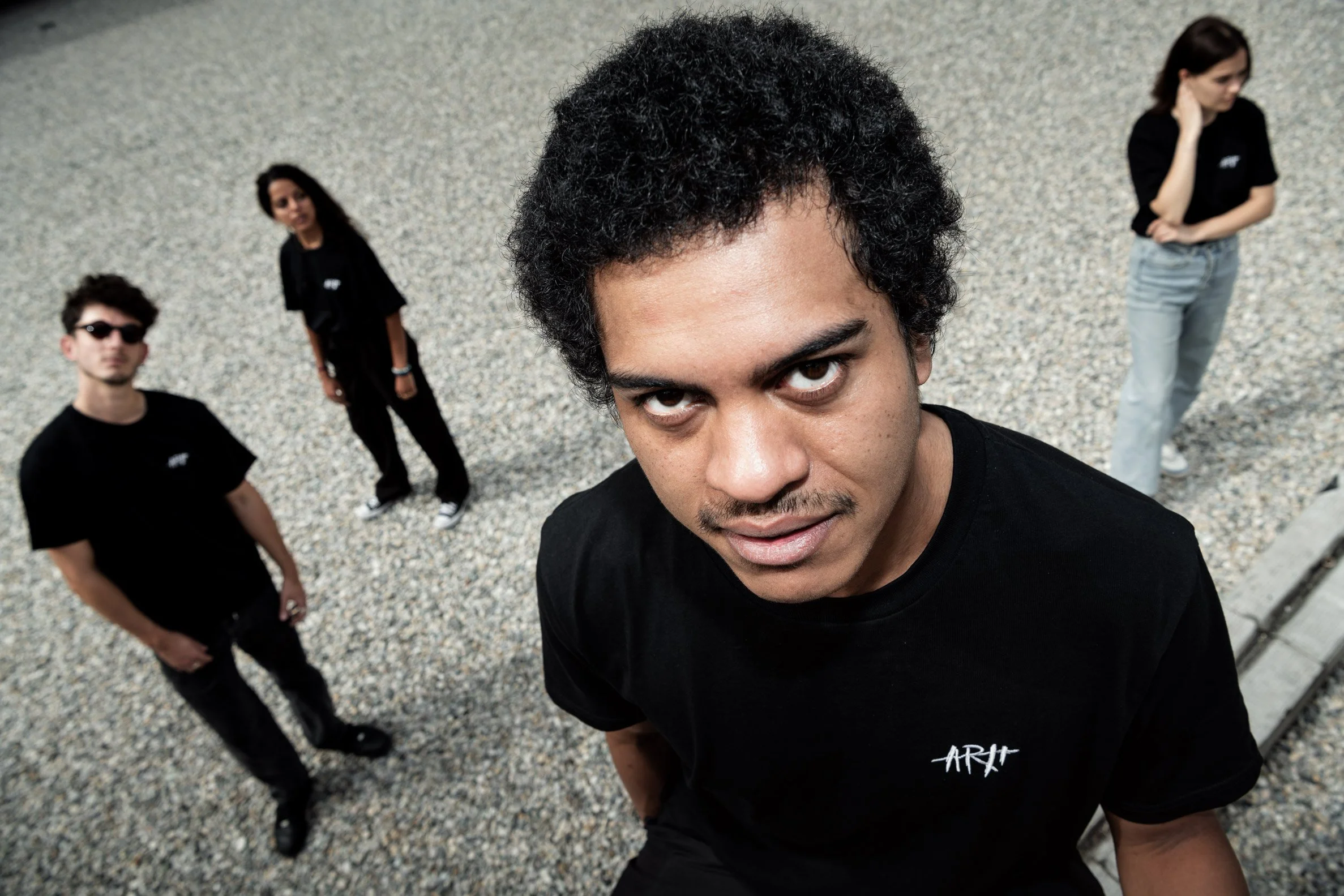 Un groupe de quatre jeunes, dont un homme au premier plan, regardant vers l'objectif, dehors sur un sol rocailleux.