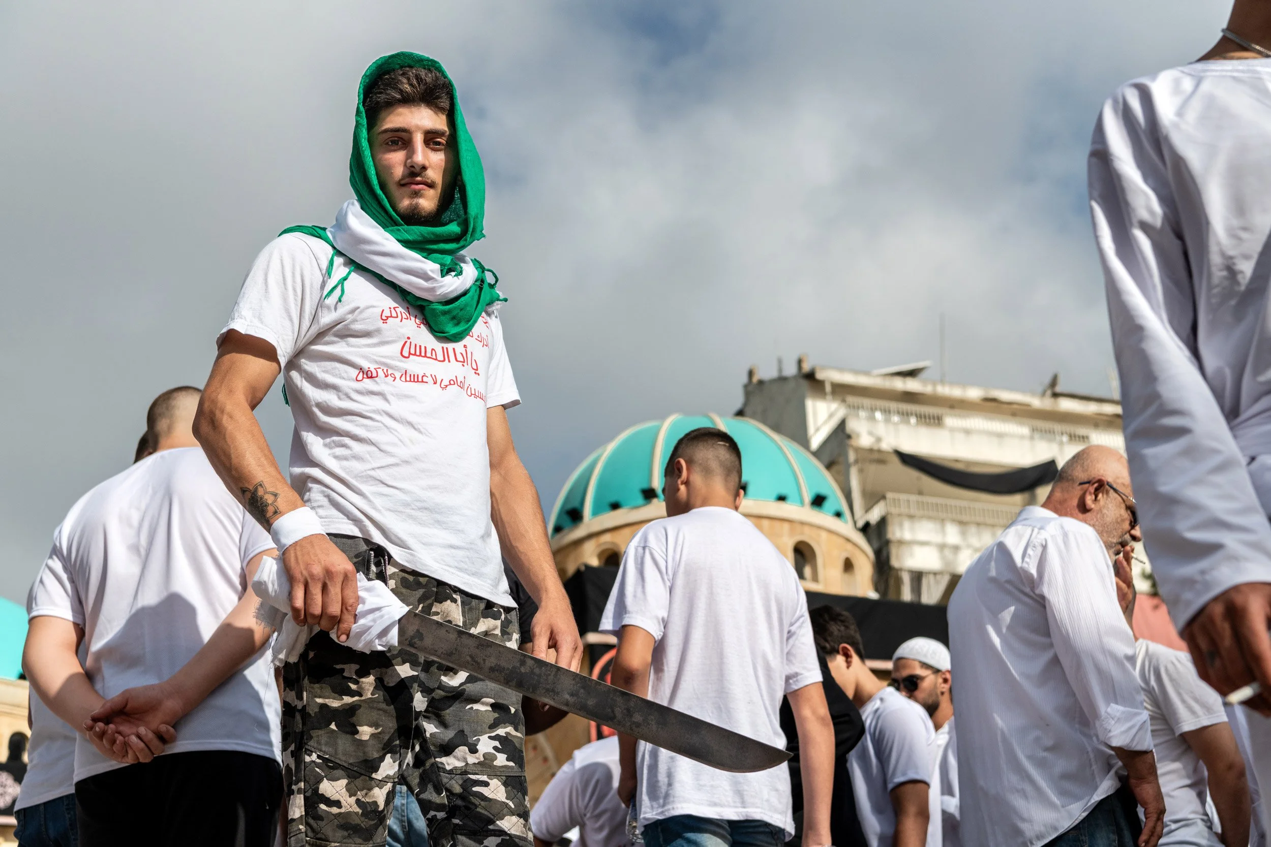 Un homme tient un sabre, utilisé par la suite pour les processions d'Ashura, pose dos  à la mosquée principale de Nabatiyeh, Liban, 29 Juillet 2023
