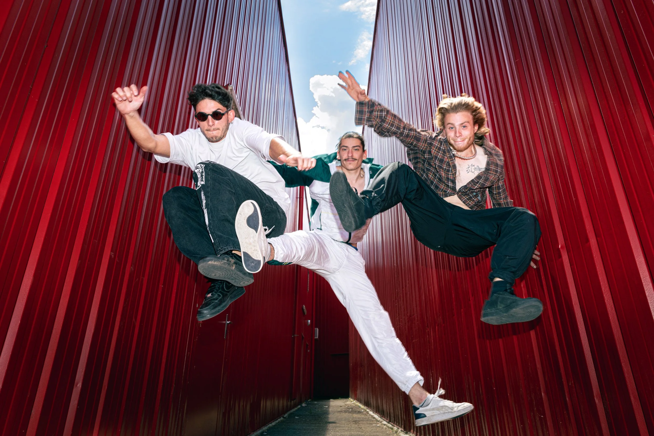 Trois jeunes hommes sautant entre deux murs rouges avec le ciel en arrière-plan.