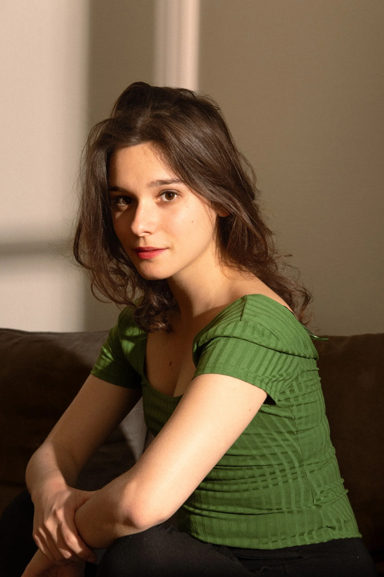 Une jeune femme aux cheveux bruns, portant un t-shirt vert, assise sur un canapé.