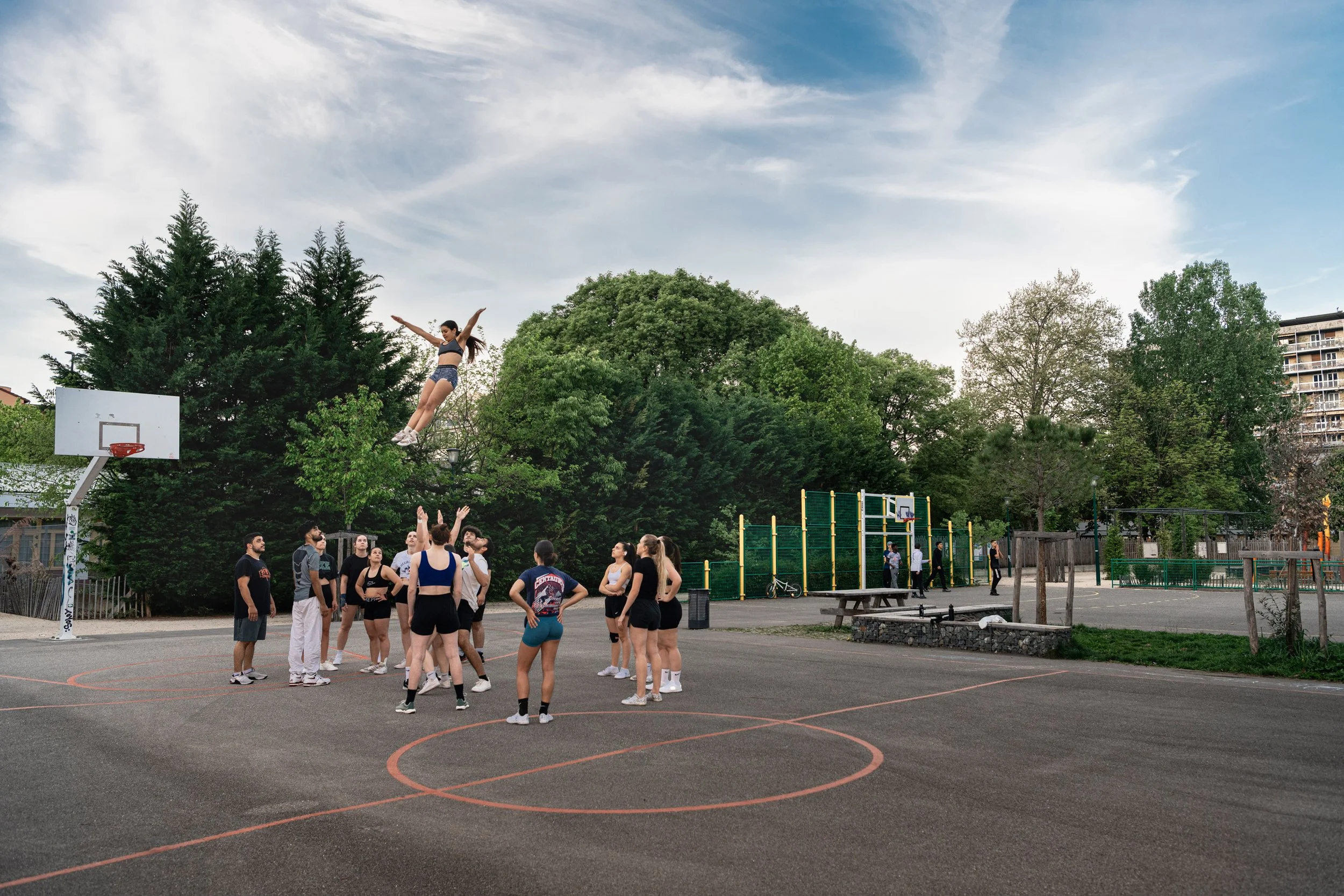 Groupe de jeunes pratiquant le cheerleading sur un terrain de basketball en plein air, avec une fille sautant dans les airs.