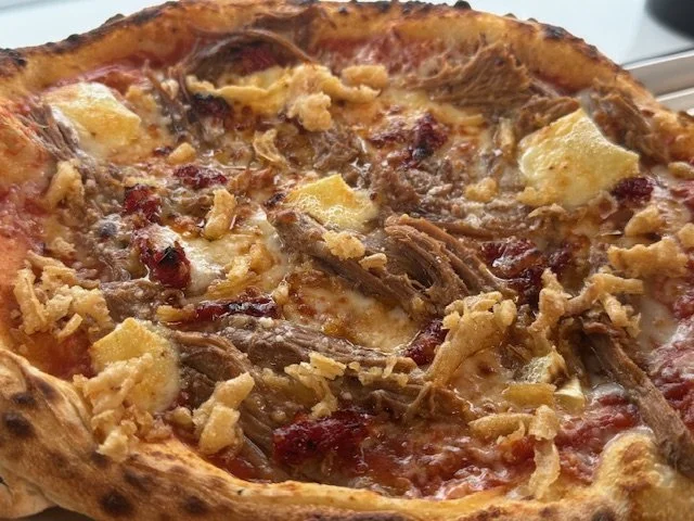 Close-up of a meat pizza with cheese, beef, and crispy fried onions on a golden crust.