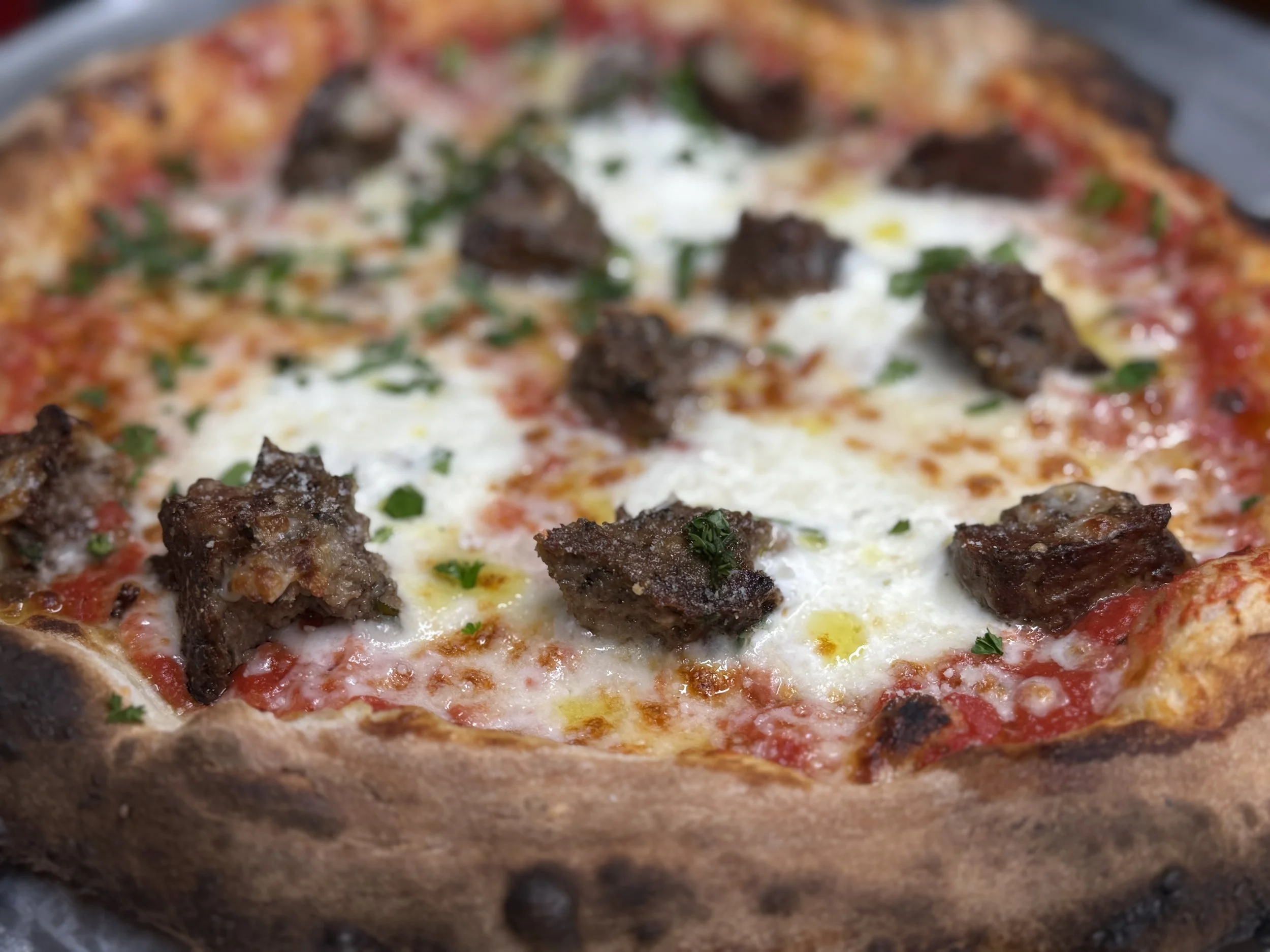 Close-up of a pizza with sausage, cheese, tomato sauce, and herbs on a thin crust.