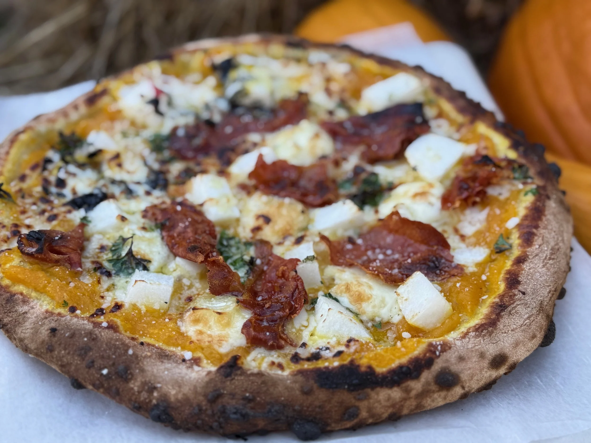 Close-up of a rustic-style pizza with bacon, cheese, and herbs on a parchment paper