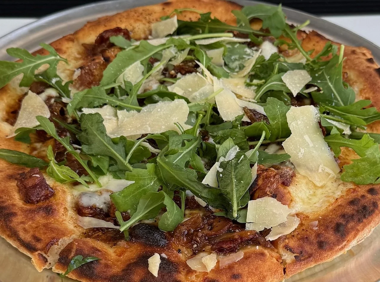 Close-up of a pizza topped with arugula, shaved Parmesan cheese, and caramelized onions, with a crispy crust.