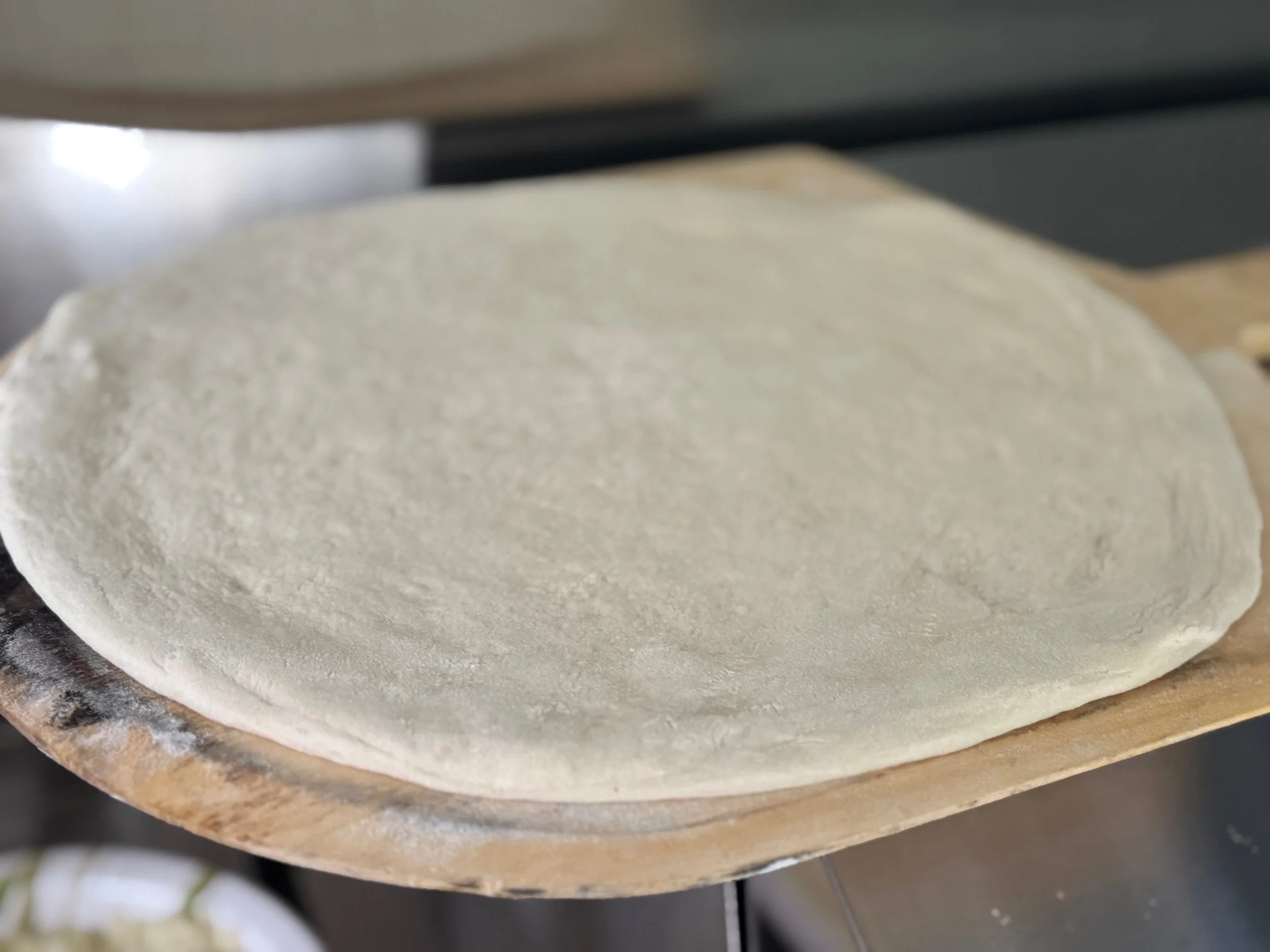Uncooked pizza dough resting on a wooden pizza peel.