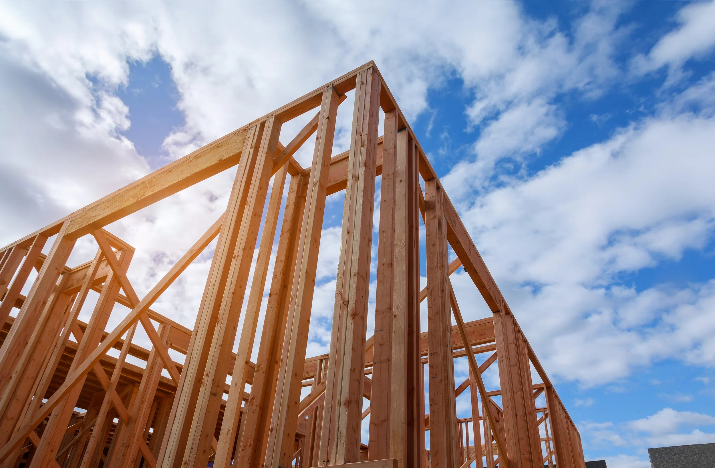 Wooden construction framing for a building against a partly cloudy blue sky.