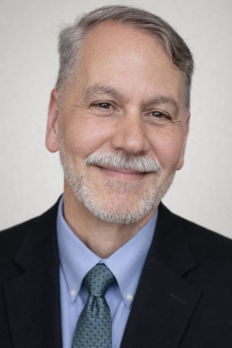 Tony Kirchmeier, A smiling man with gray hair and a beard, wearing a dark suit, light blue dress shirt, and patterned tie.