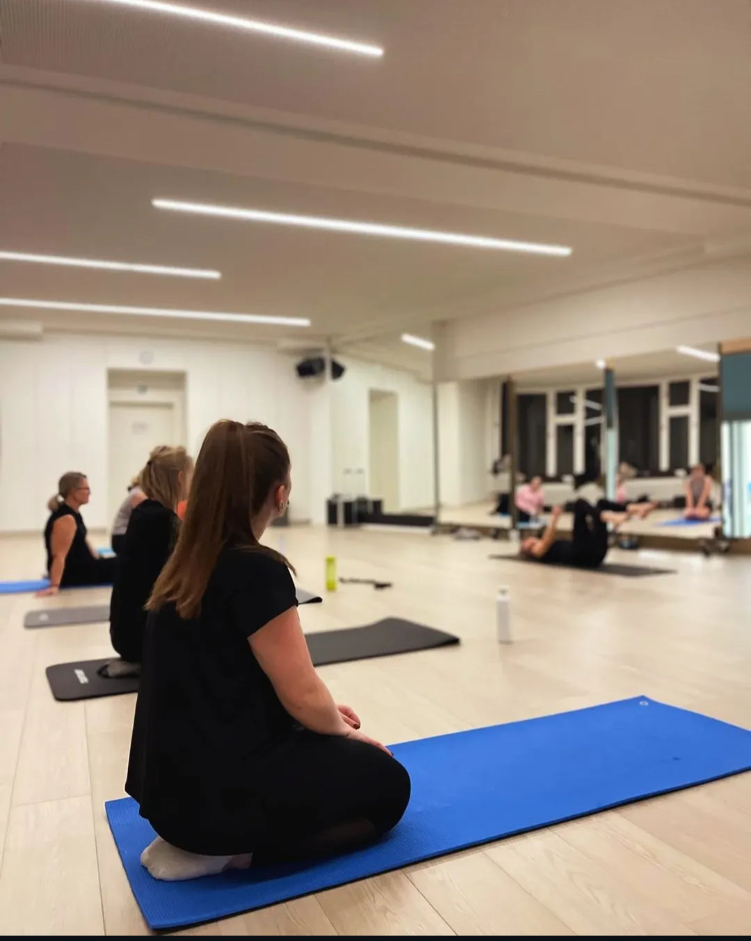 Group of women practicing core stability training on mats in a spacious, well-lit studio.