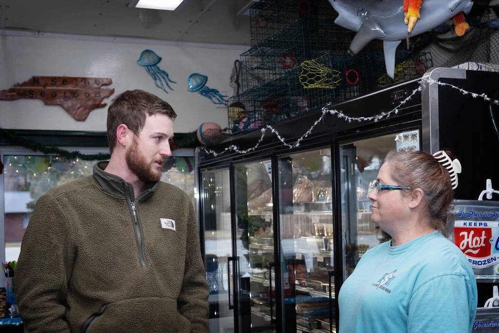 A man and a woman talking inside a store, with a display case and fish decoration in the background.