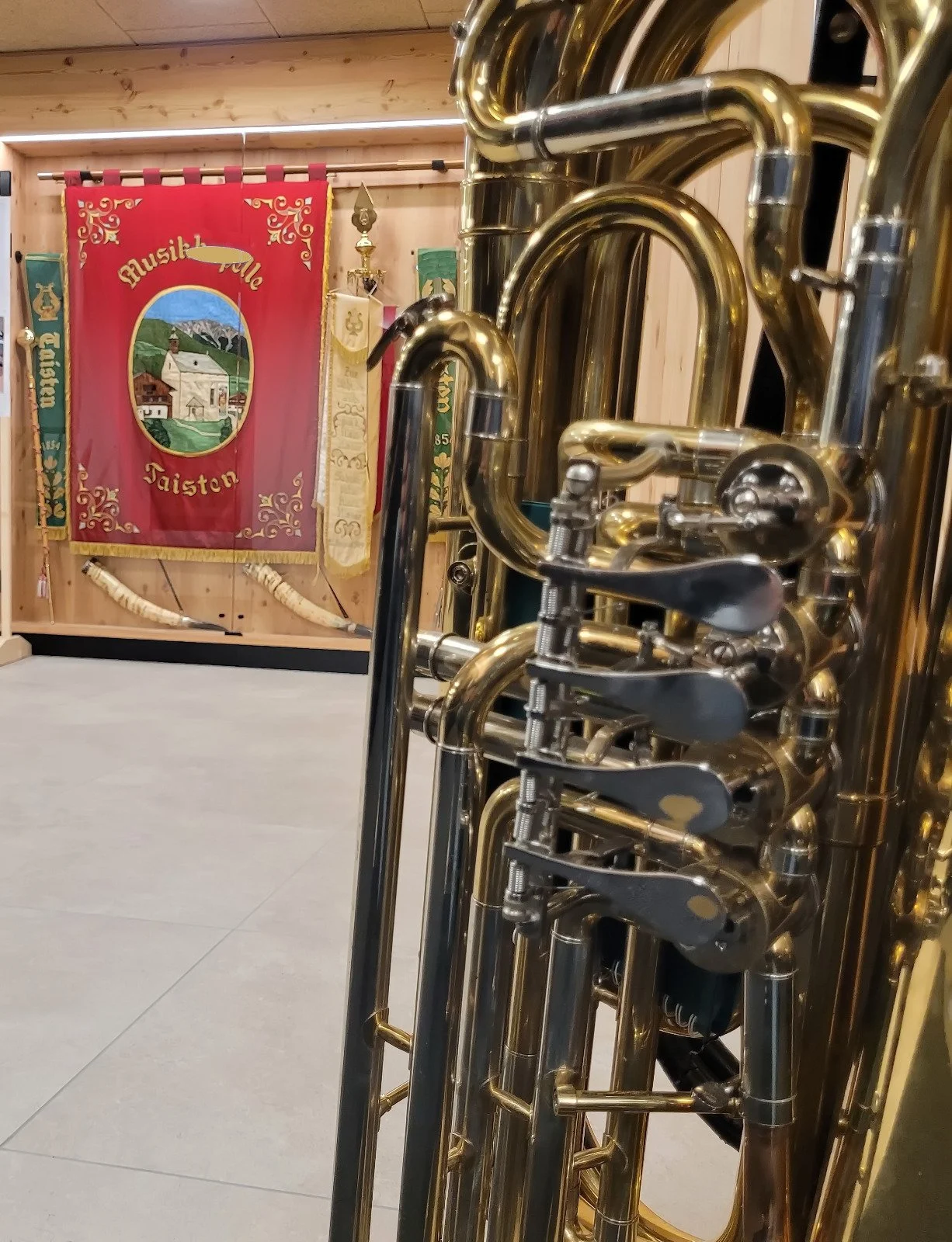 Mehrere goldene Saxofone stehen nebeneinander in einem Musikraum, im Hintergrund gibt es eine rote Fahne mit einem gemalten Bild und den Worten ‚Musik Tale Tasten‘.