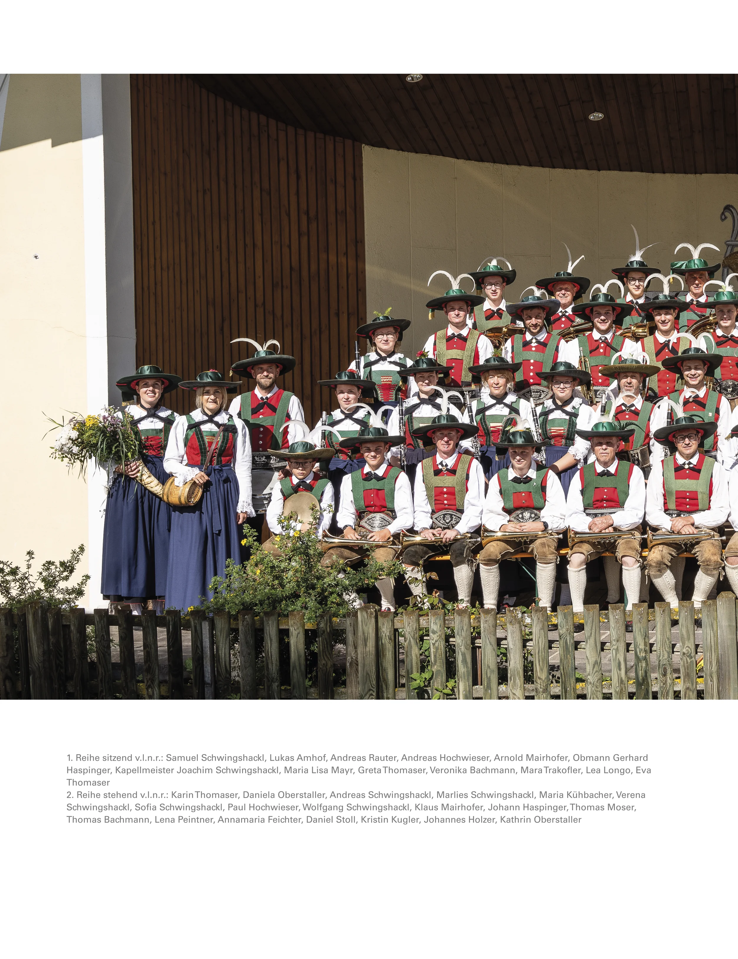 Gruppe von Musikern in traditionellen bayerischen Trachten mit Hut und Feder, die auf einer Bühne stehen.