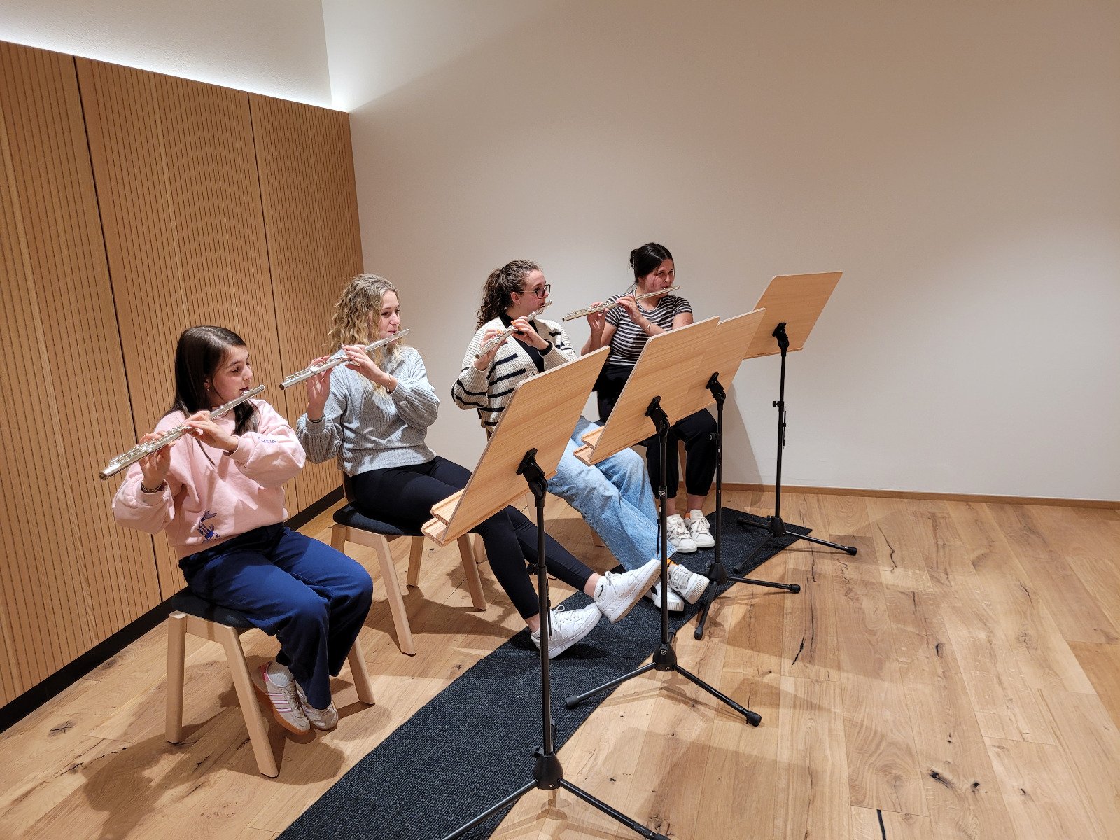 Vier junge Frauen spielen Flöte in einem Raum mit Holzboot und Notenständern.