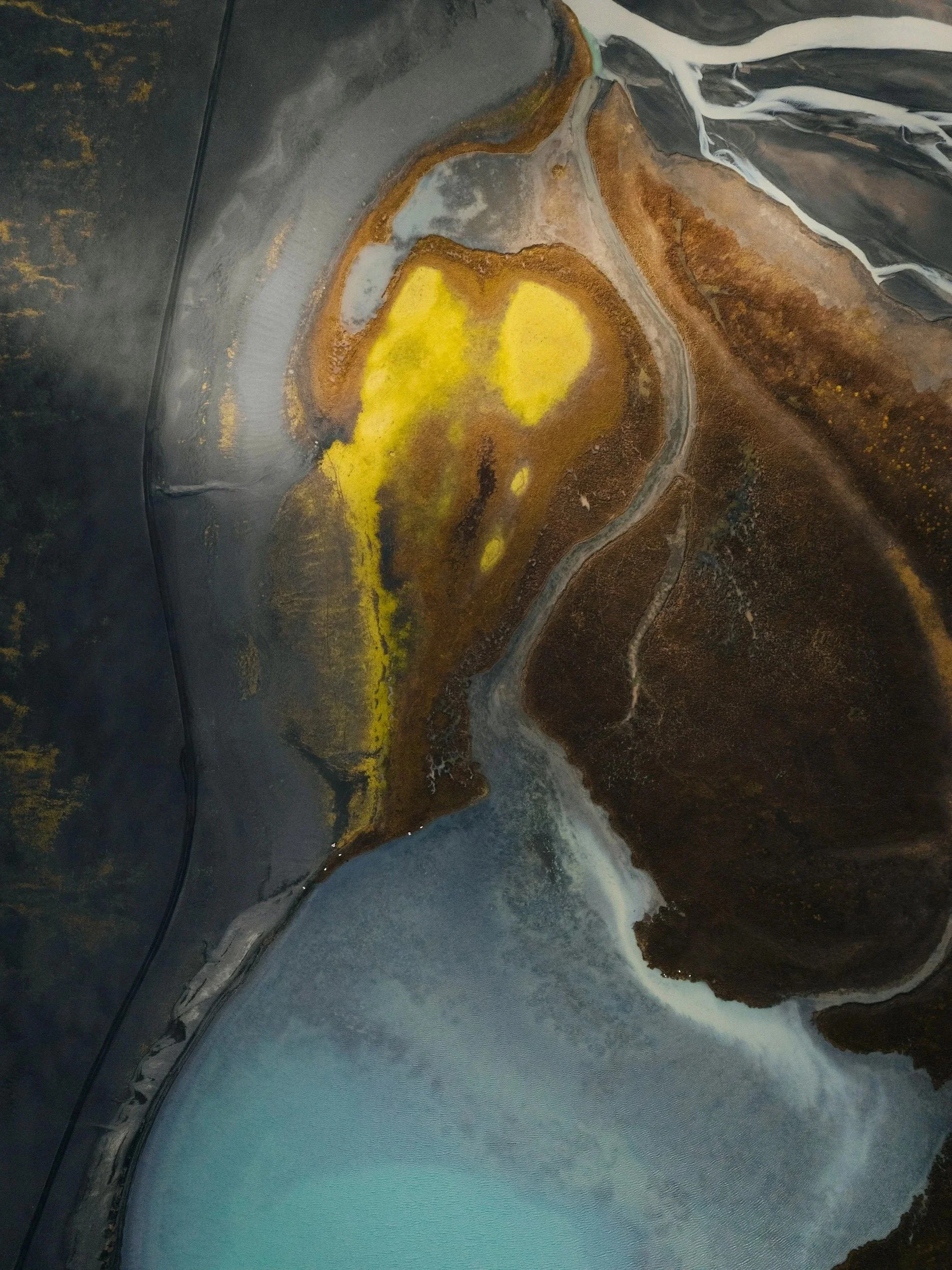 Abstract aerial view of a landscape with a mix of dark, brown, yellow, and turquoise colors, resembling land and water formations.