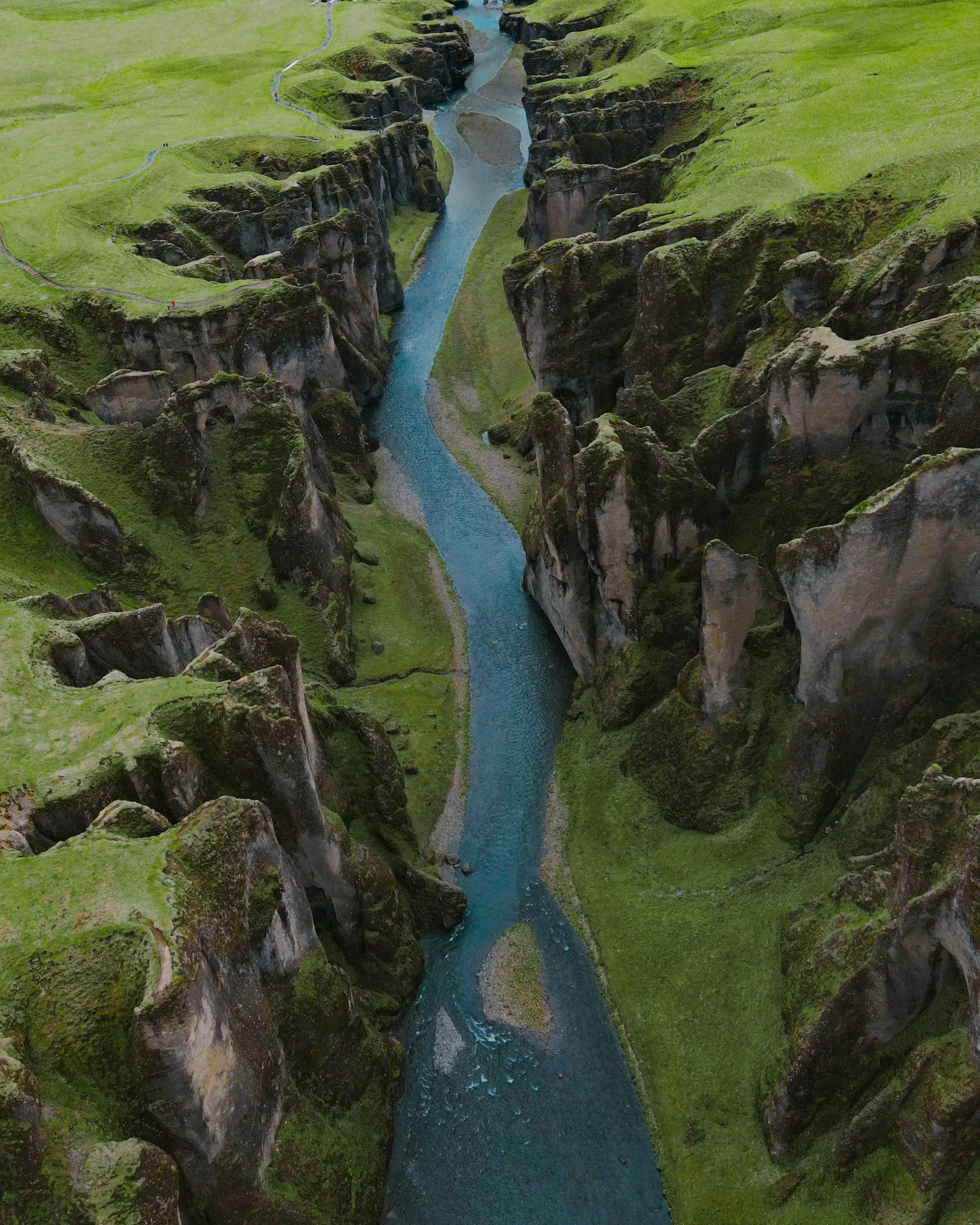 Aerial view of a canyon with steep green grassy cliffs and a winding blue river running through the bottom.