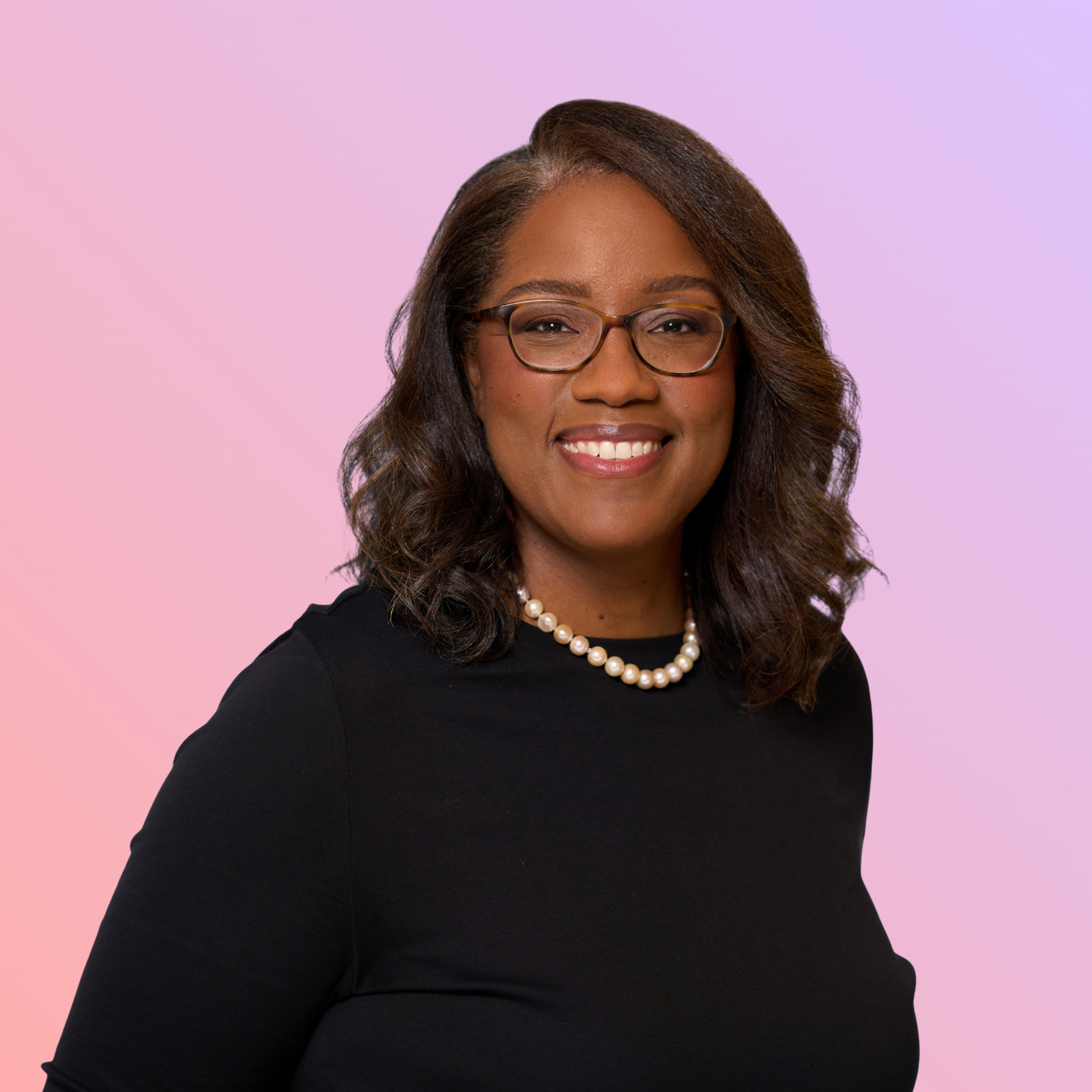 Portrait of a smiling woman with glasses, curly hair, wearing a black top and pearl necklace, against a peach and purple gradient background.
