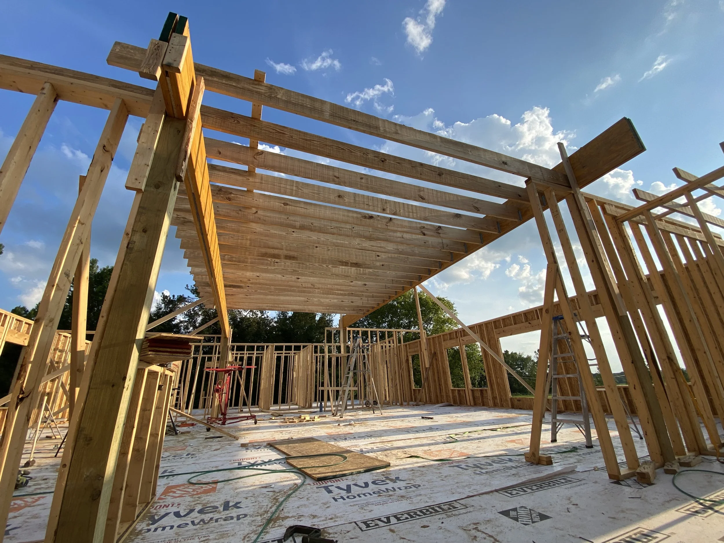 Construction site with wooden framing and partially built ceiling under a partly cloudy sky.