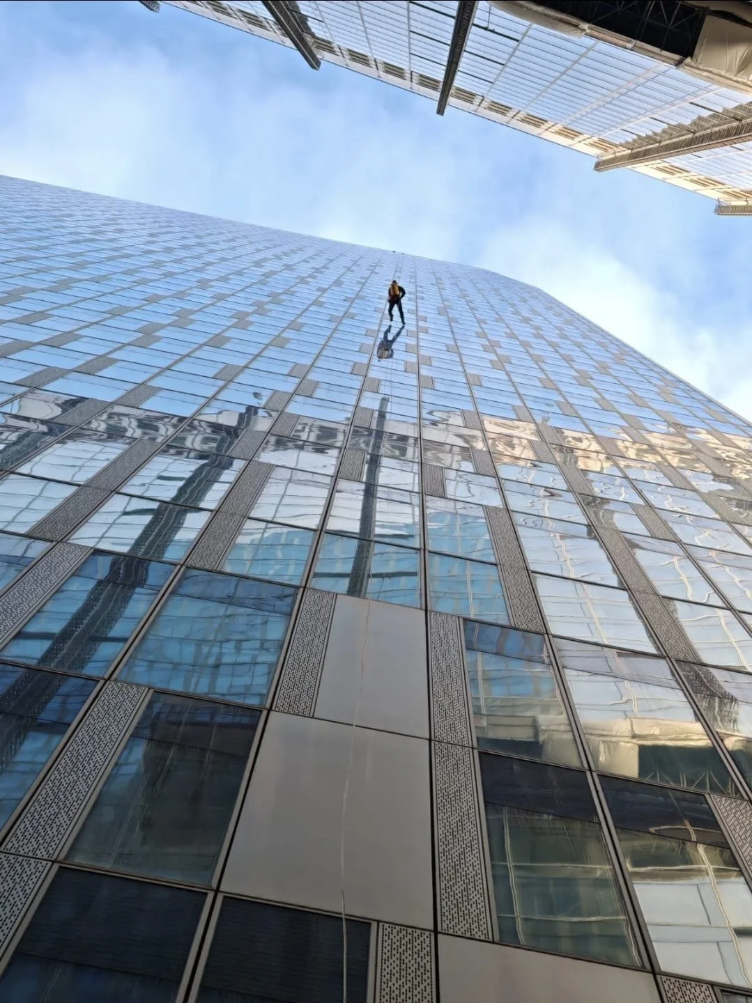 Un grimpeur nettoie la façade d'un grand bâtiment en verre dans une ville moderne.