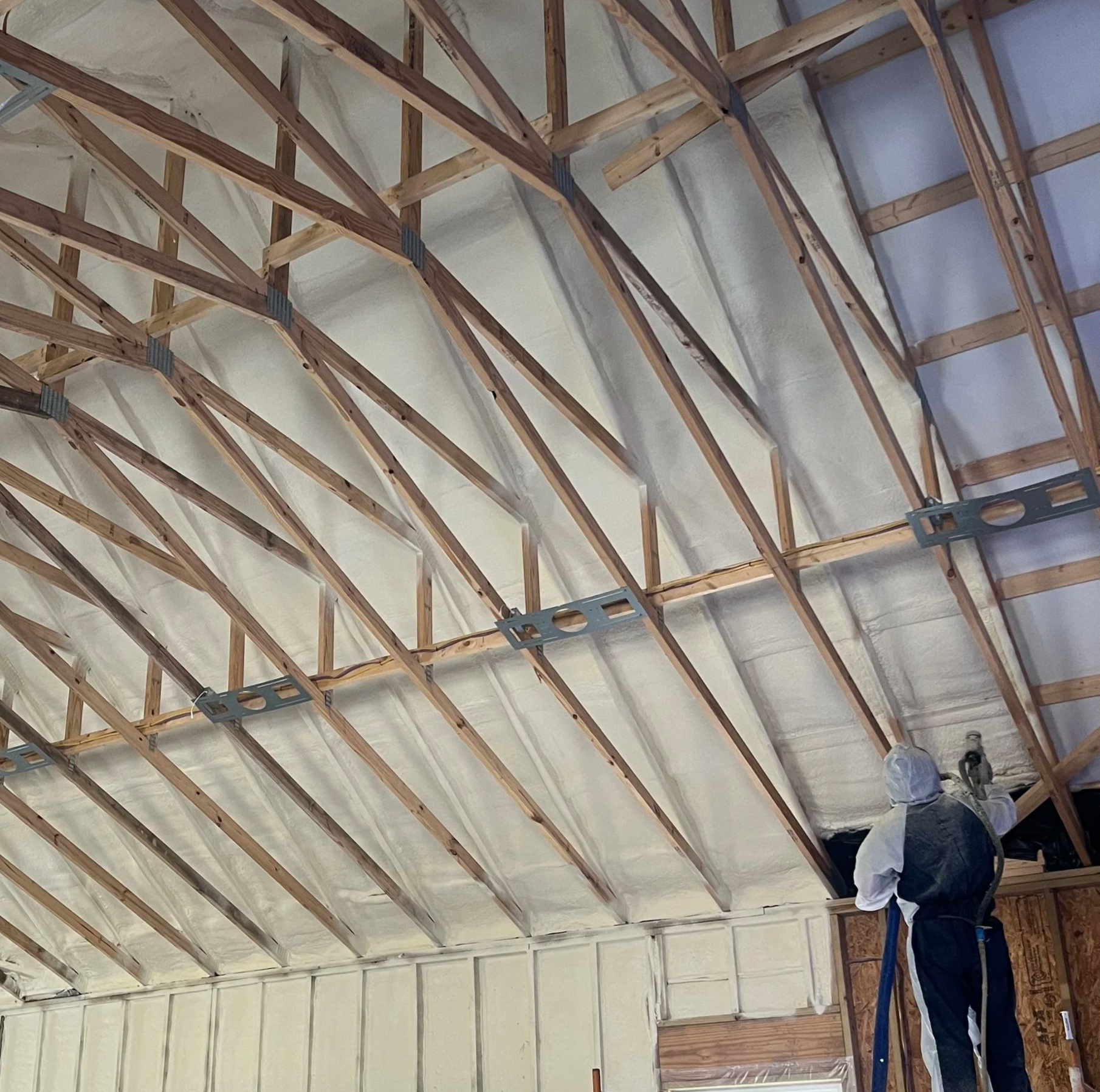 A construction worker installing insulation in the ceiling of a building with exposed wooden beams.