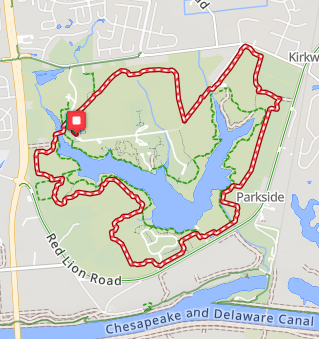 Map of a park trail around a large water body, with a red trail line and surrounding streets including Red Lion Road and Chesapeake and Delaware Canal.