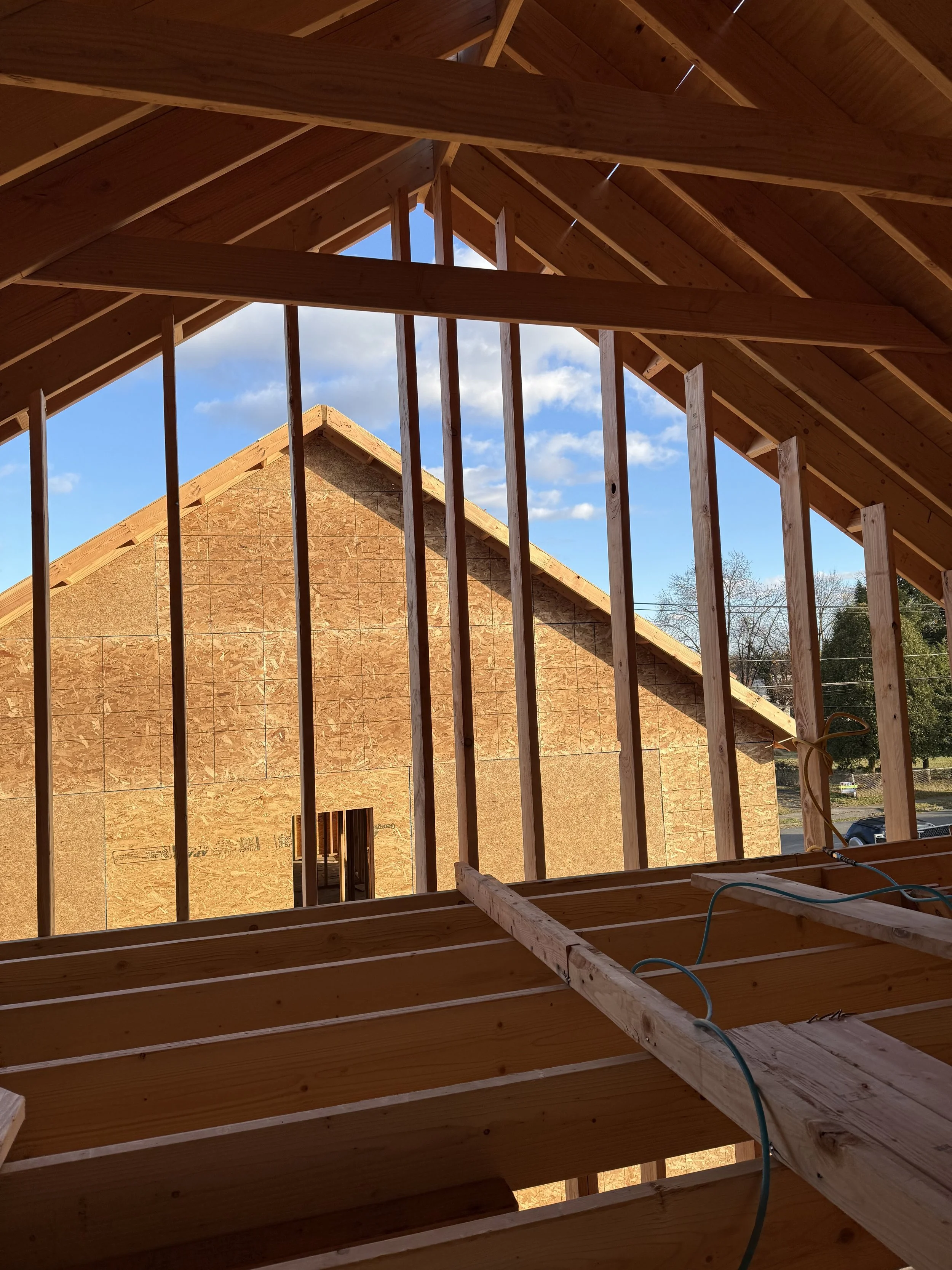 View from inside a wooden house under construction, showing roof framing and exterior sheathing of nearby building.