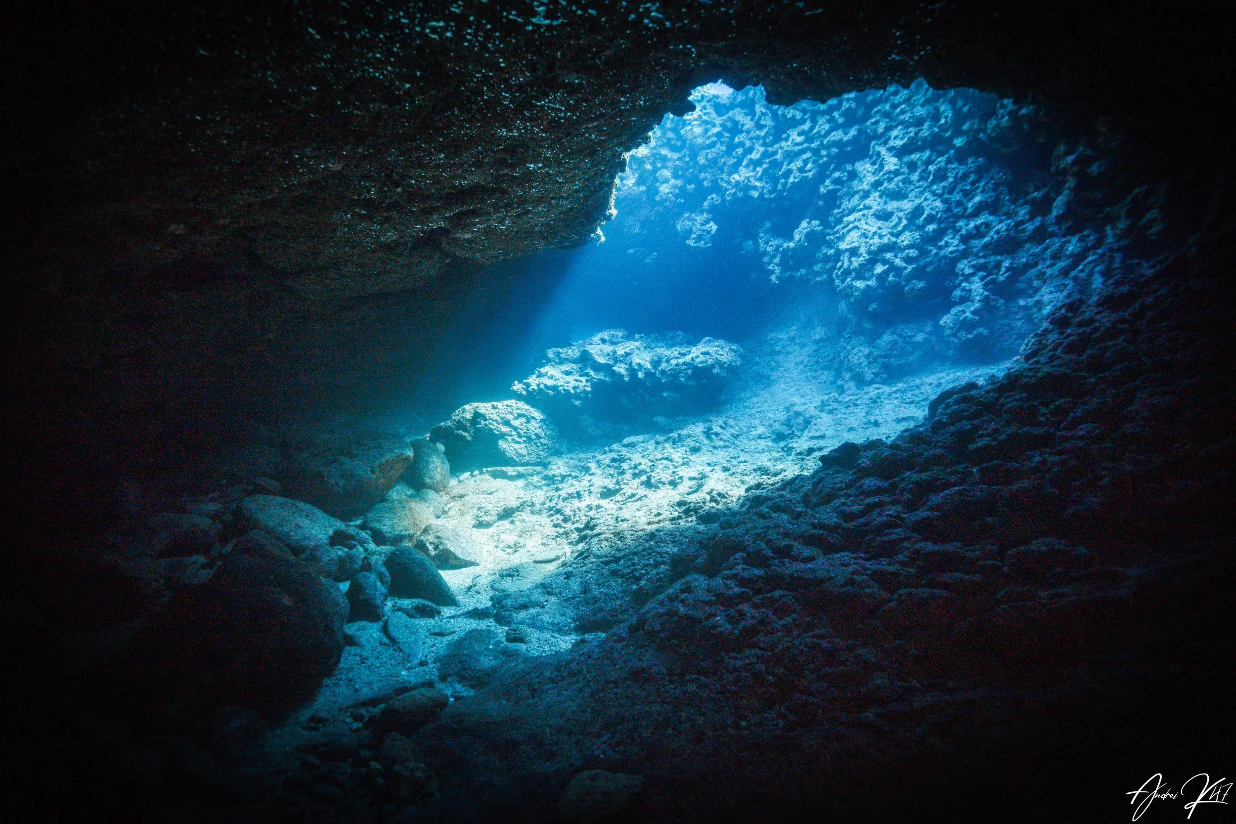 Underwater cave illuminated by sunlight streaming through an opening, showing rocky walls and sandy seabed near Protaras, Cyprus.