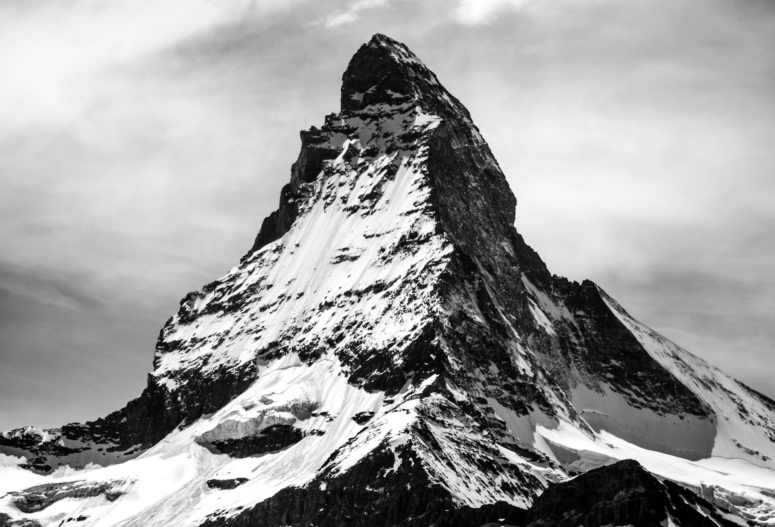 A black-and-white photograph of a tall, snow-covered mountain with a pointed peak, likely a famous mountain such as the Matterhorn.