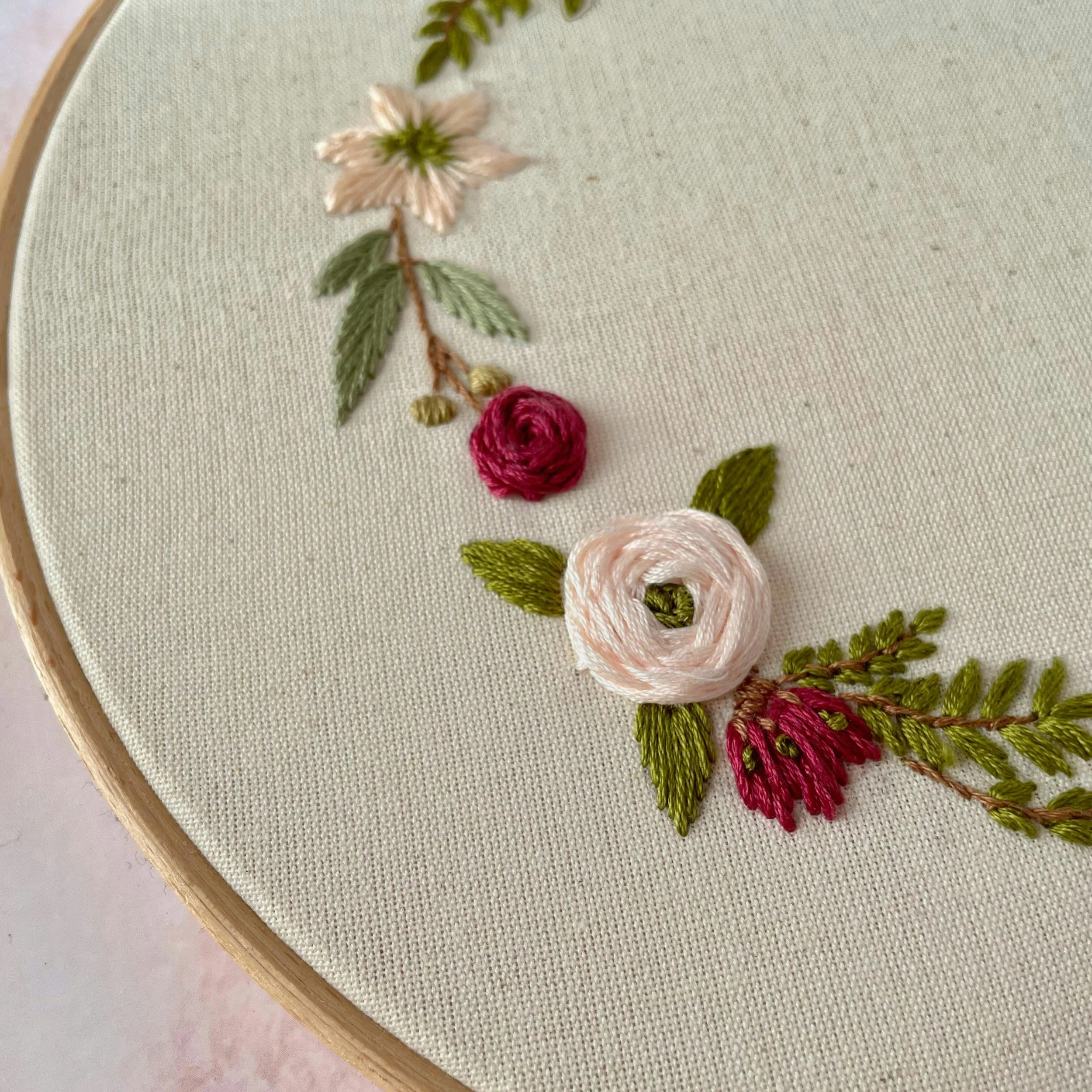 Embroidery of pink, white, and red flowers with green leaves on white fabric in an embroidery hoop.