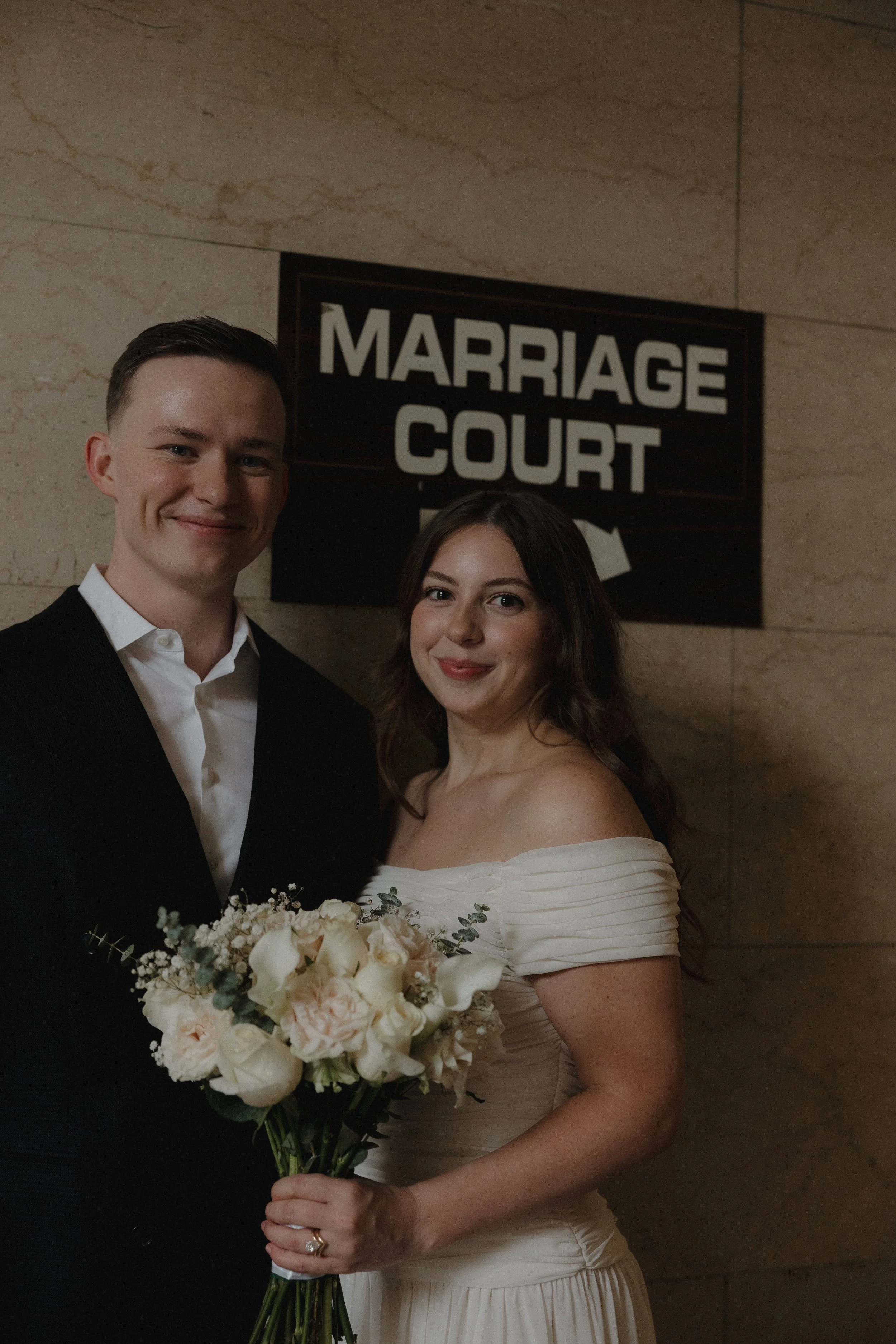 a young couple after their court house wedding posing in front of the marriage court sign