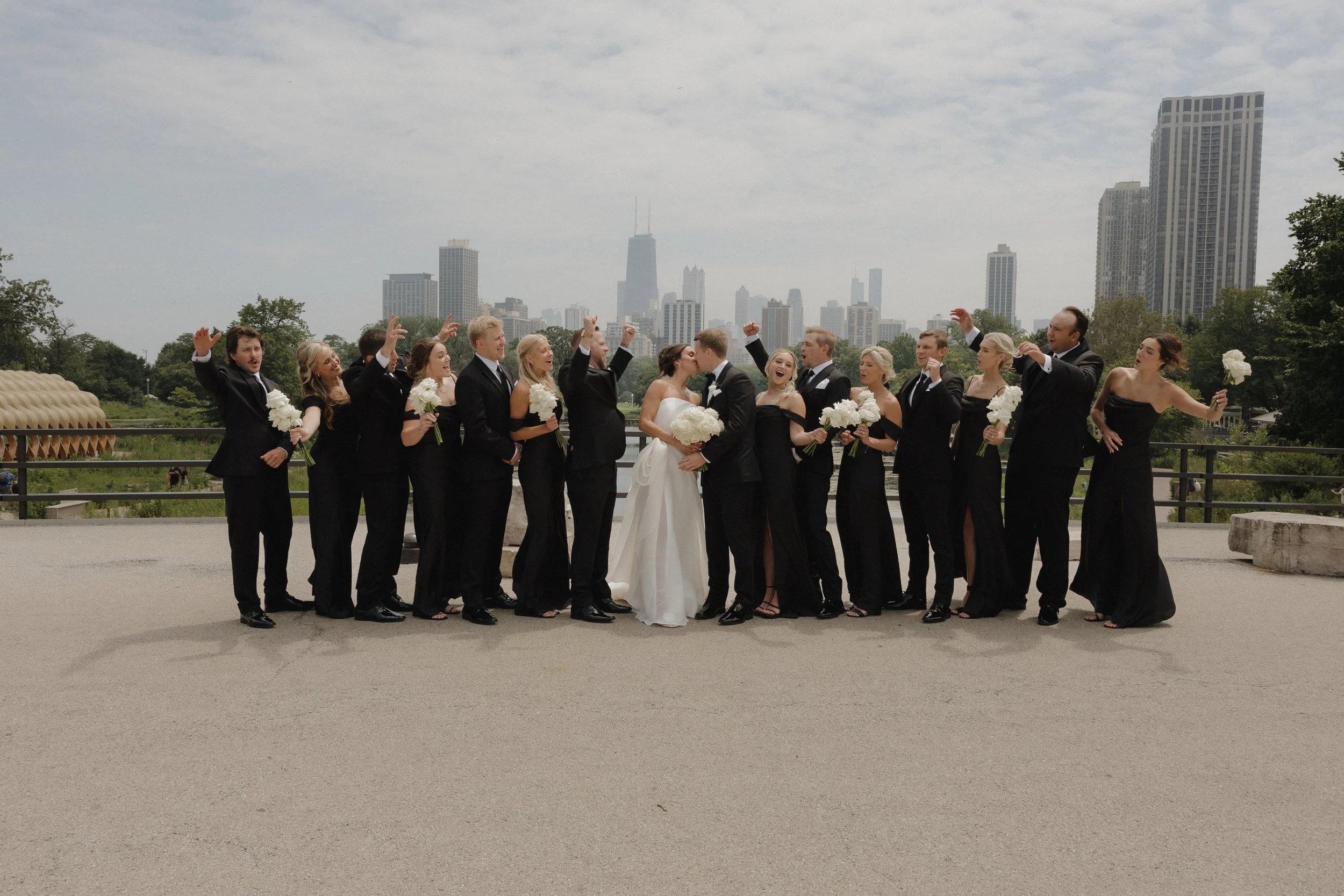 A wedding party cheering as the couple kisses in the middle of them