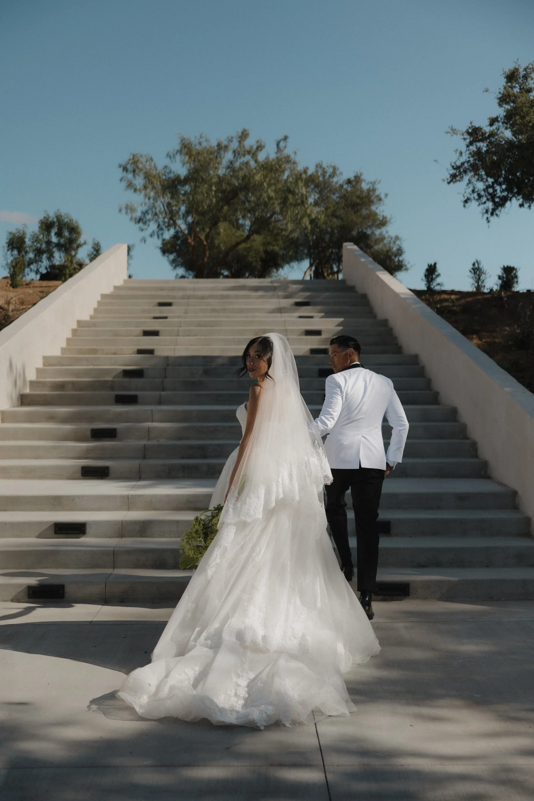 A bride and groom walking up some steps at their venue and looking back at the camera while the groom looks back at his bride 