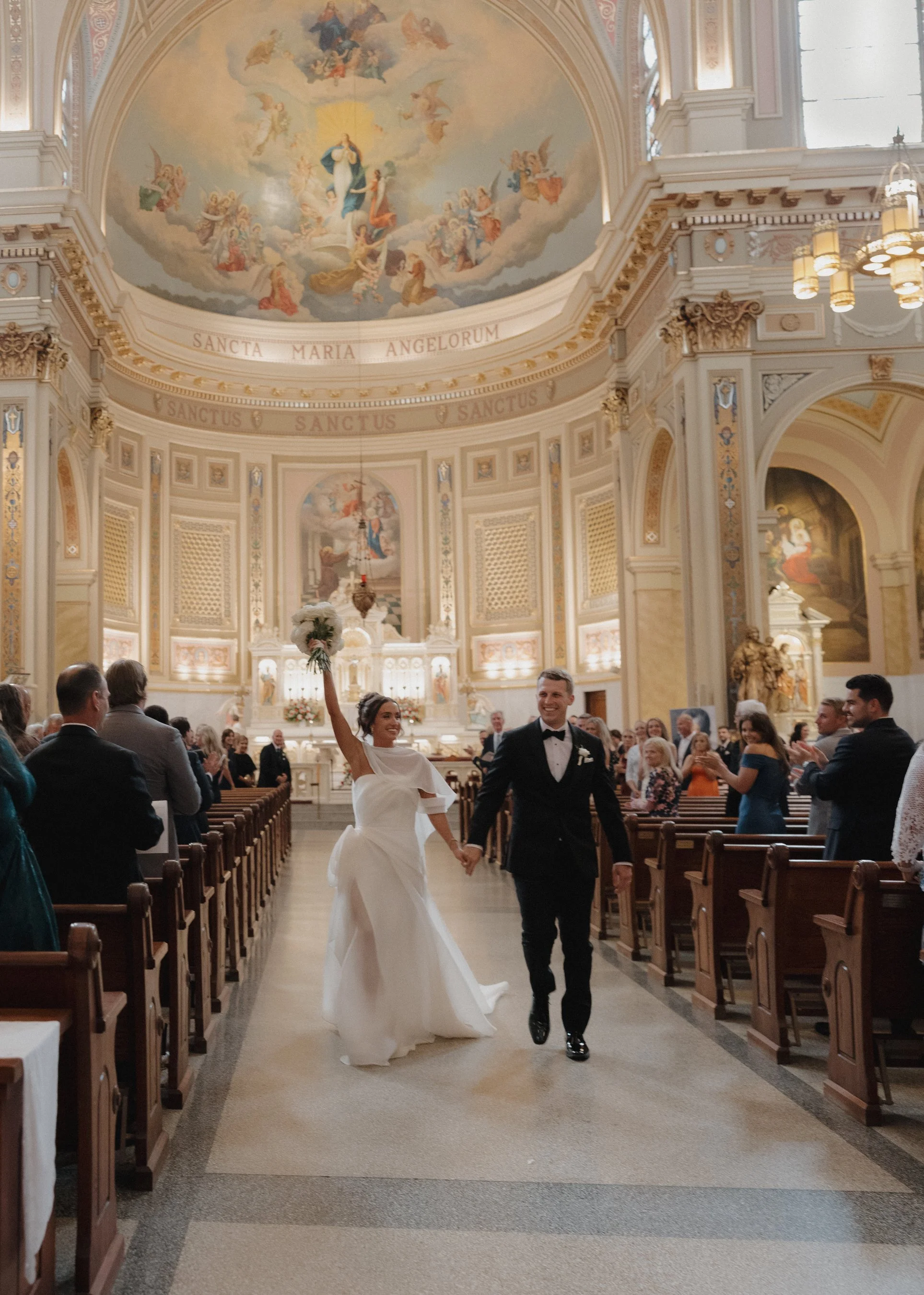 A young couple walking away after their ceremony while their guest all cheer for them behind them