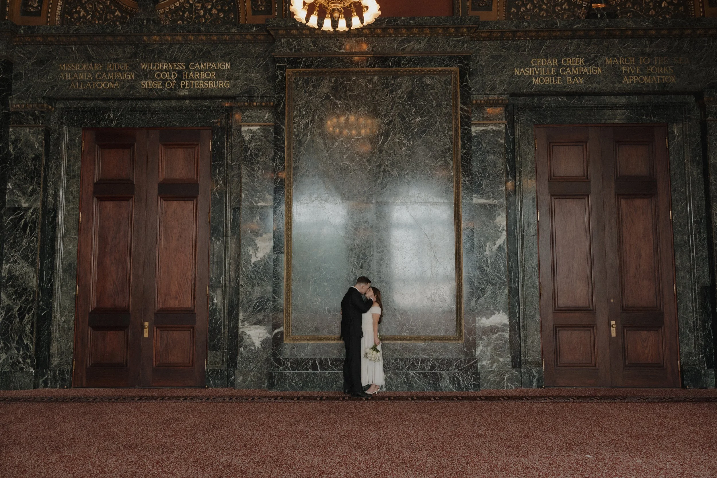 A young bride and groom kissing and embracing eachother in a wide shot at cultural center in Chicago, IL