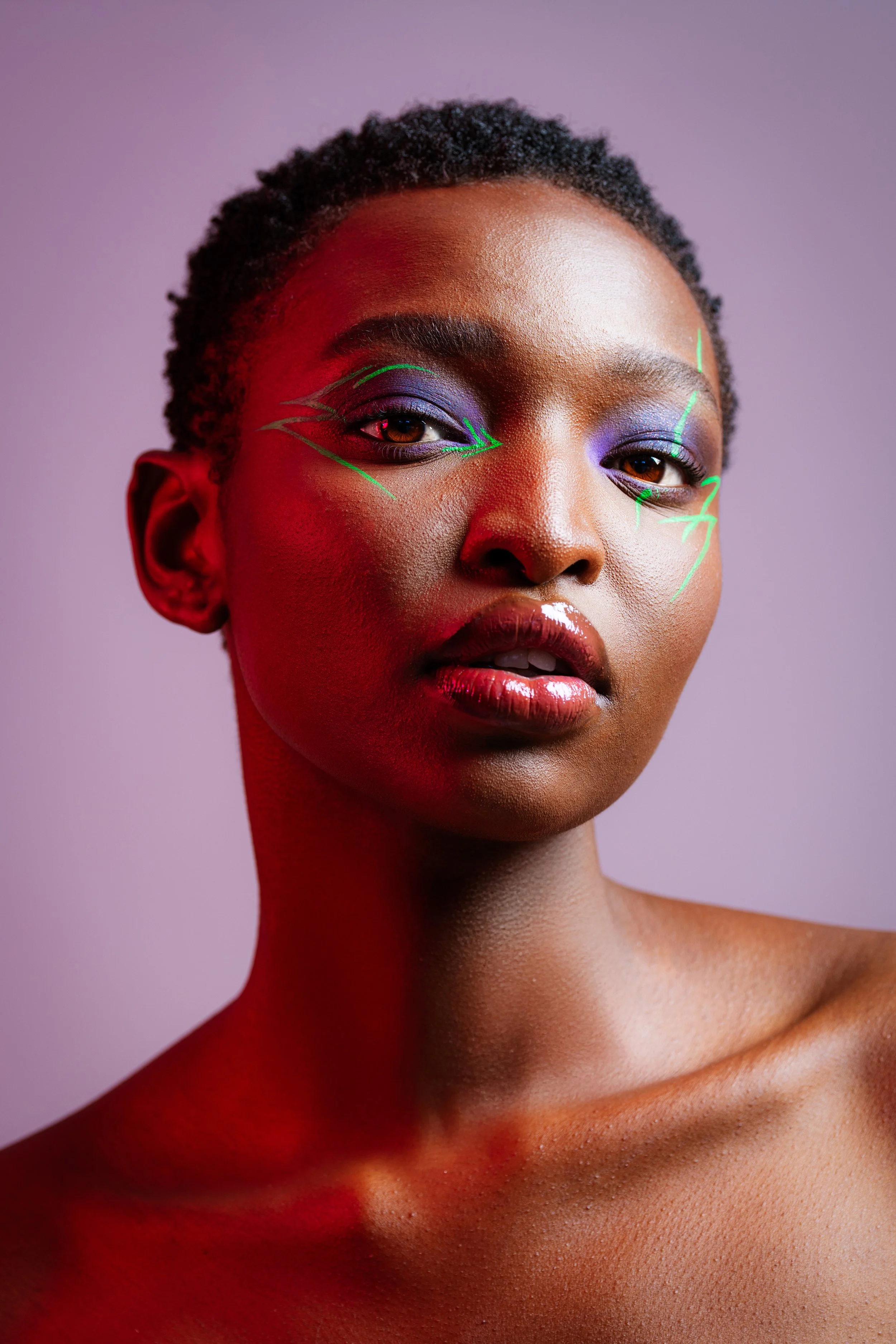 Portrait of a woman with vibrant makeup and neon facial lines on pink and purple background.