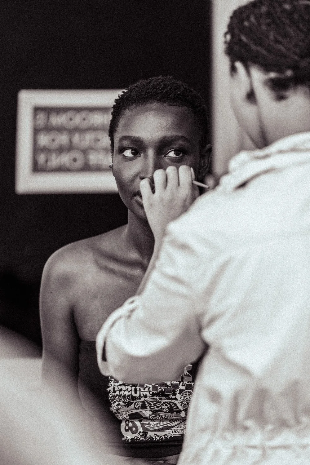 A woman getting her makeup done by a makeup artist in a black and white photo.
