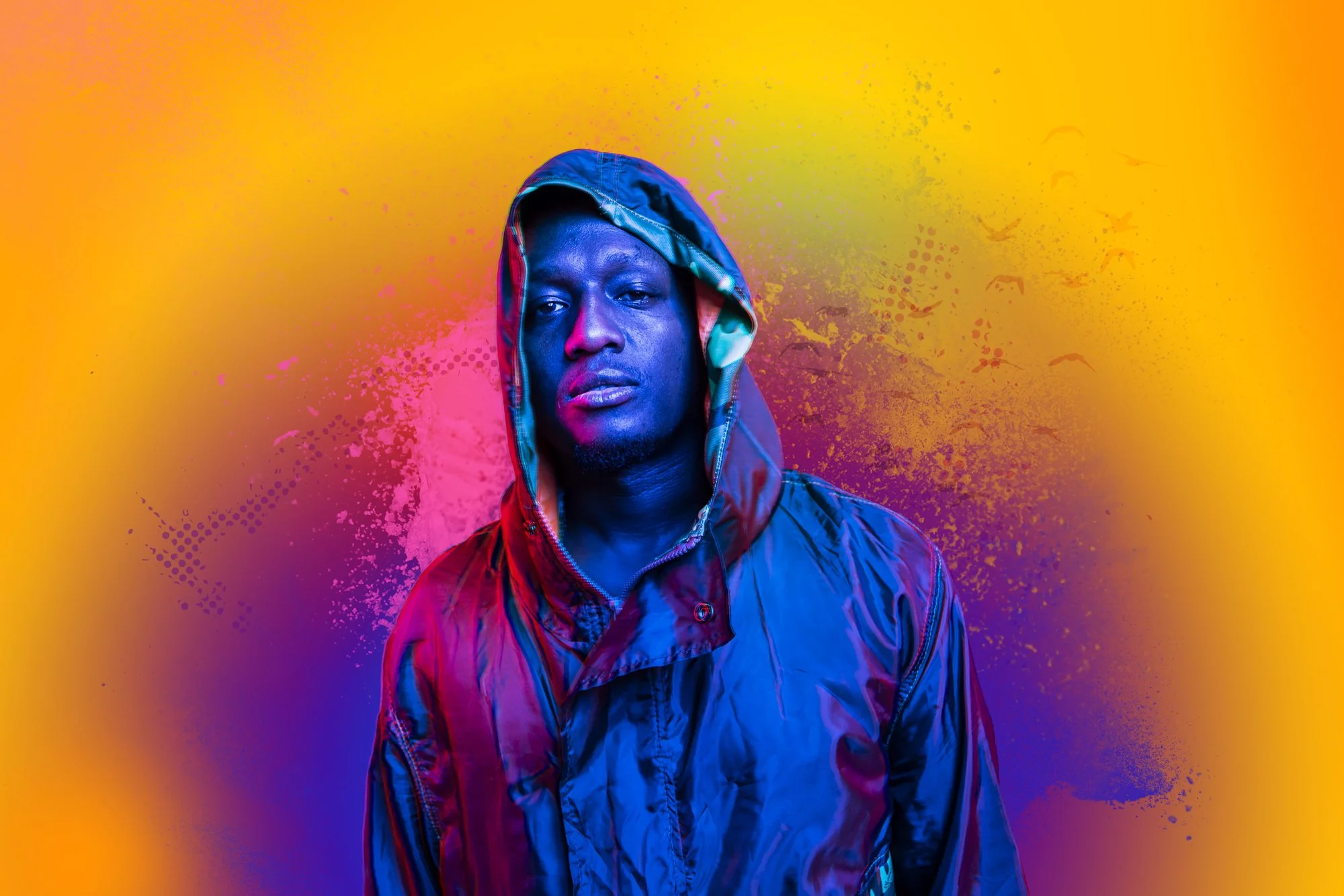 A man wearing a colorful hooded jacket against a vibrant, abstract background with yellow, pink, purple, and green splashes.